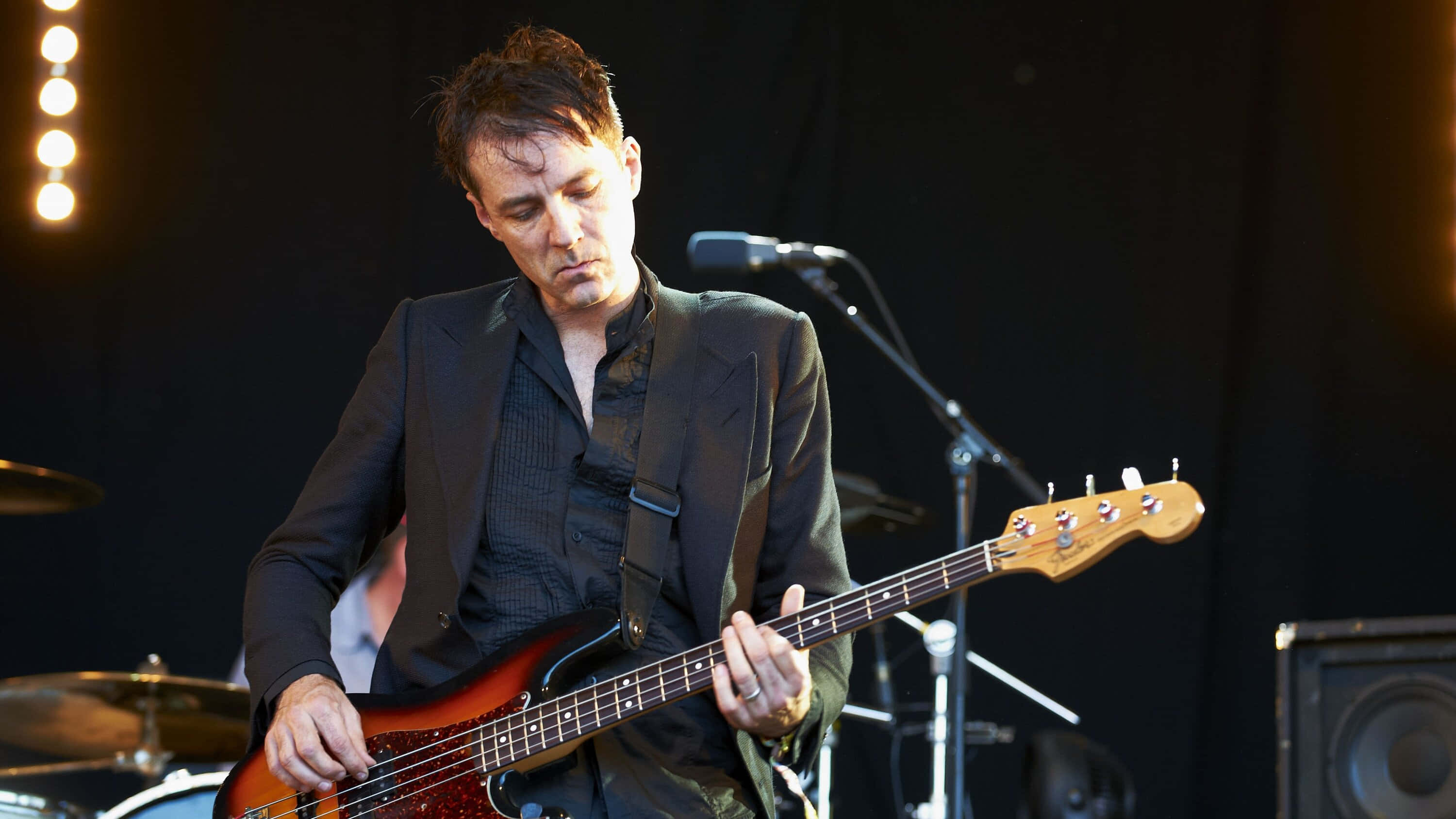 Steve Mackey, sunburst bass guitar, dimly lit stage, 2K Desktop Wallpaper