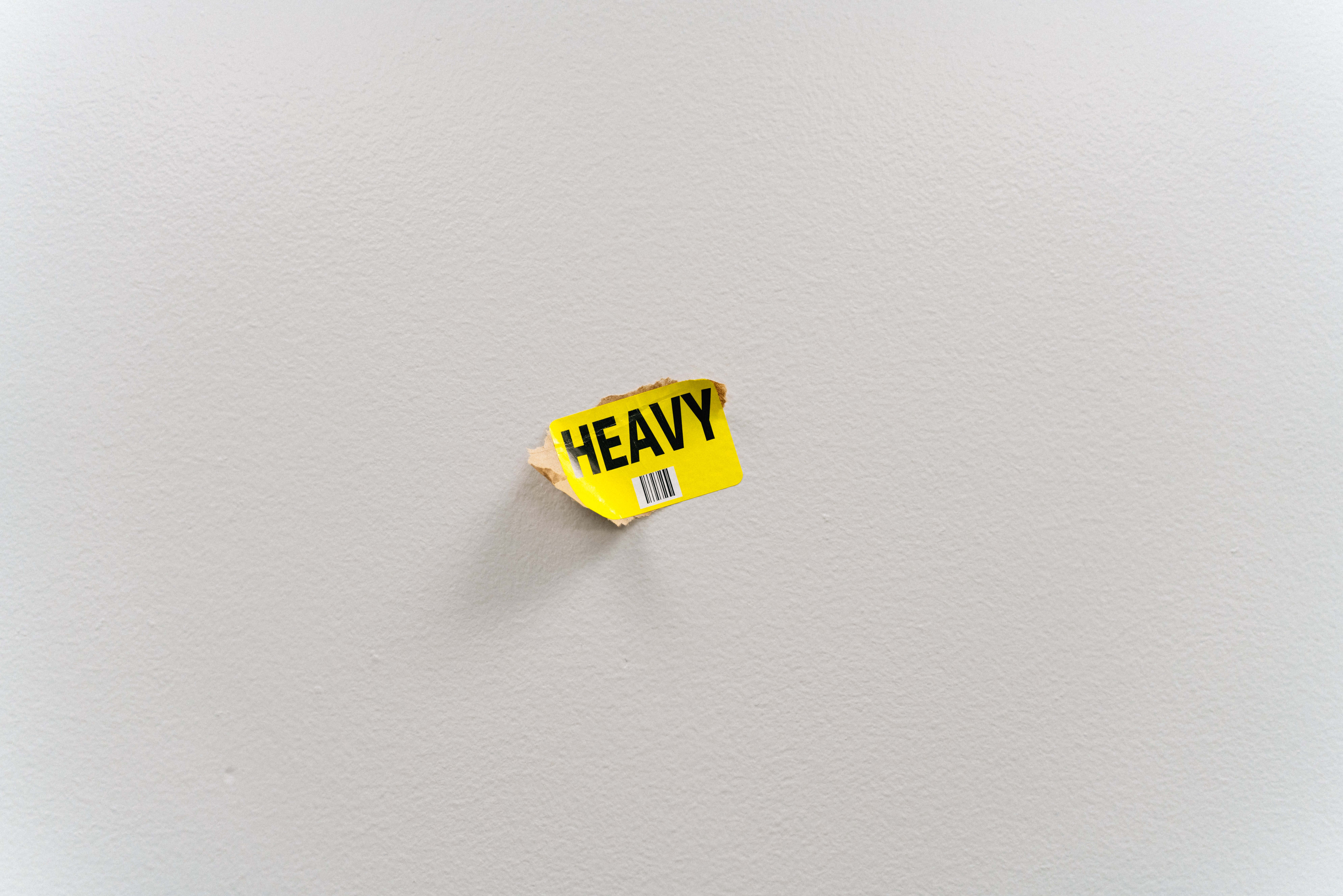 HEAVY, torn yellow shipping label, plain white textured wall, 8K Desktop Wallpaper