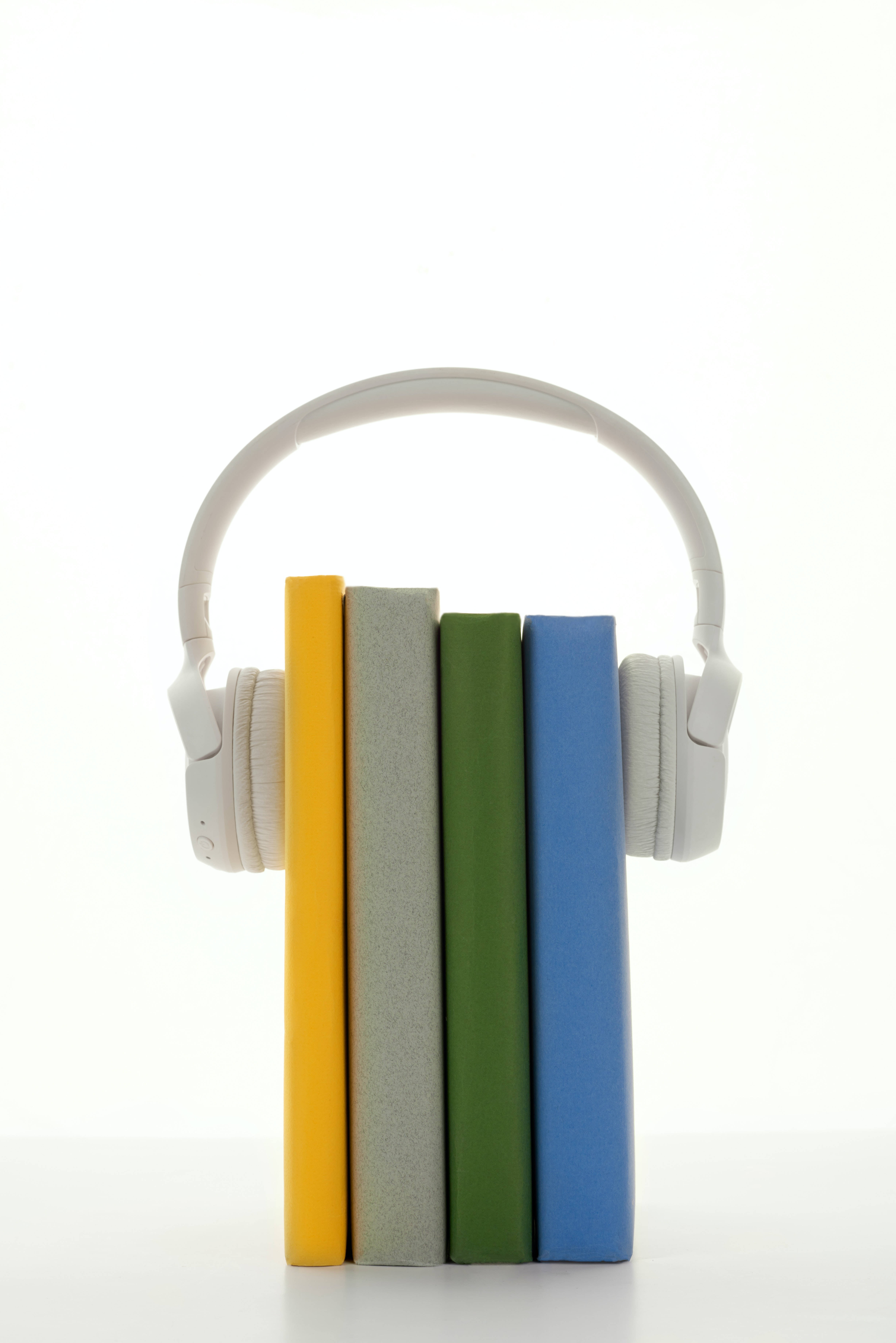 white over-ear headphones, four vertically aligned colorful books, clean white background, 5K Phone Wallpaper