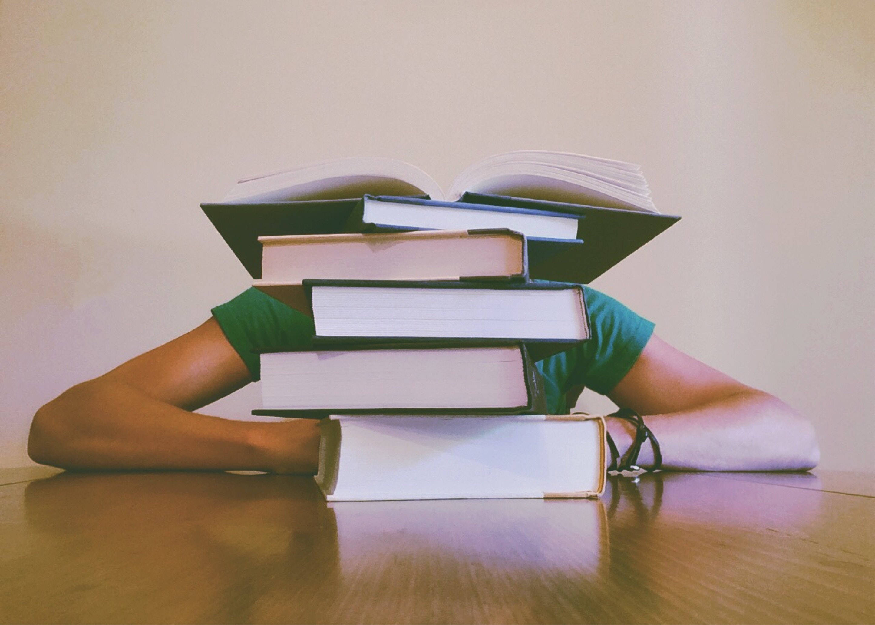 green shirt, tall stack of books, wooden desk, 2K Desktop Wallpaper