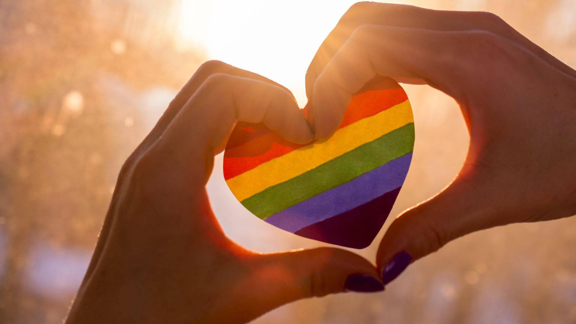 rainbow flag heart cutout, glowing sunset backdrop, hands forming a heart shape, Full HD Desktop Wallpaper