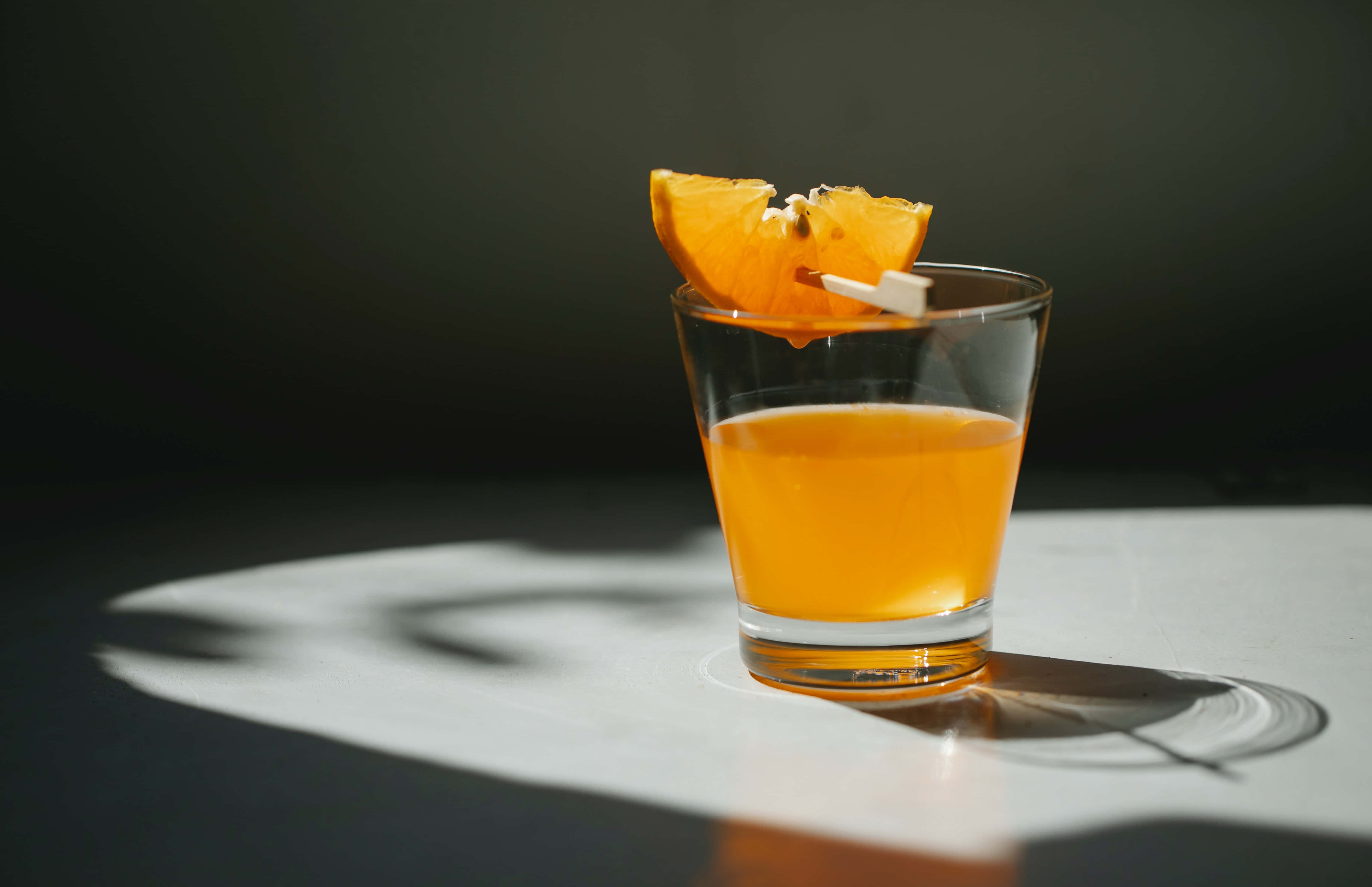 amber cocktail, orange slice garnish, white surface, 4K Desktop Wallpaper