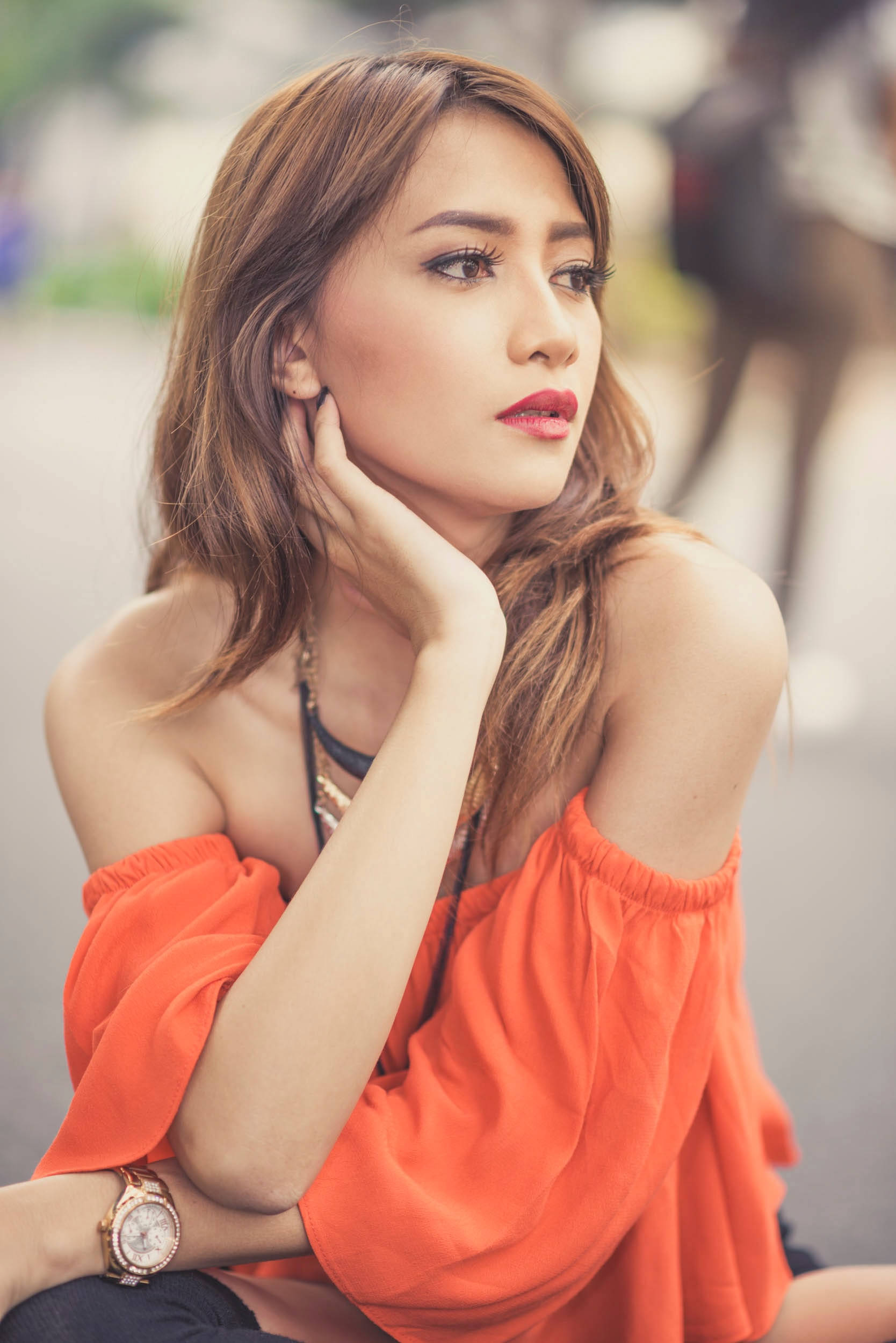 female model, vibrant orange off-shoulder top, softly blurred urban background, Full HD Phone Wallpaper