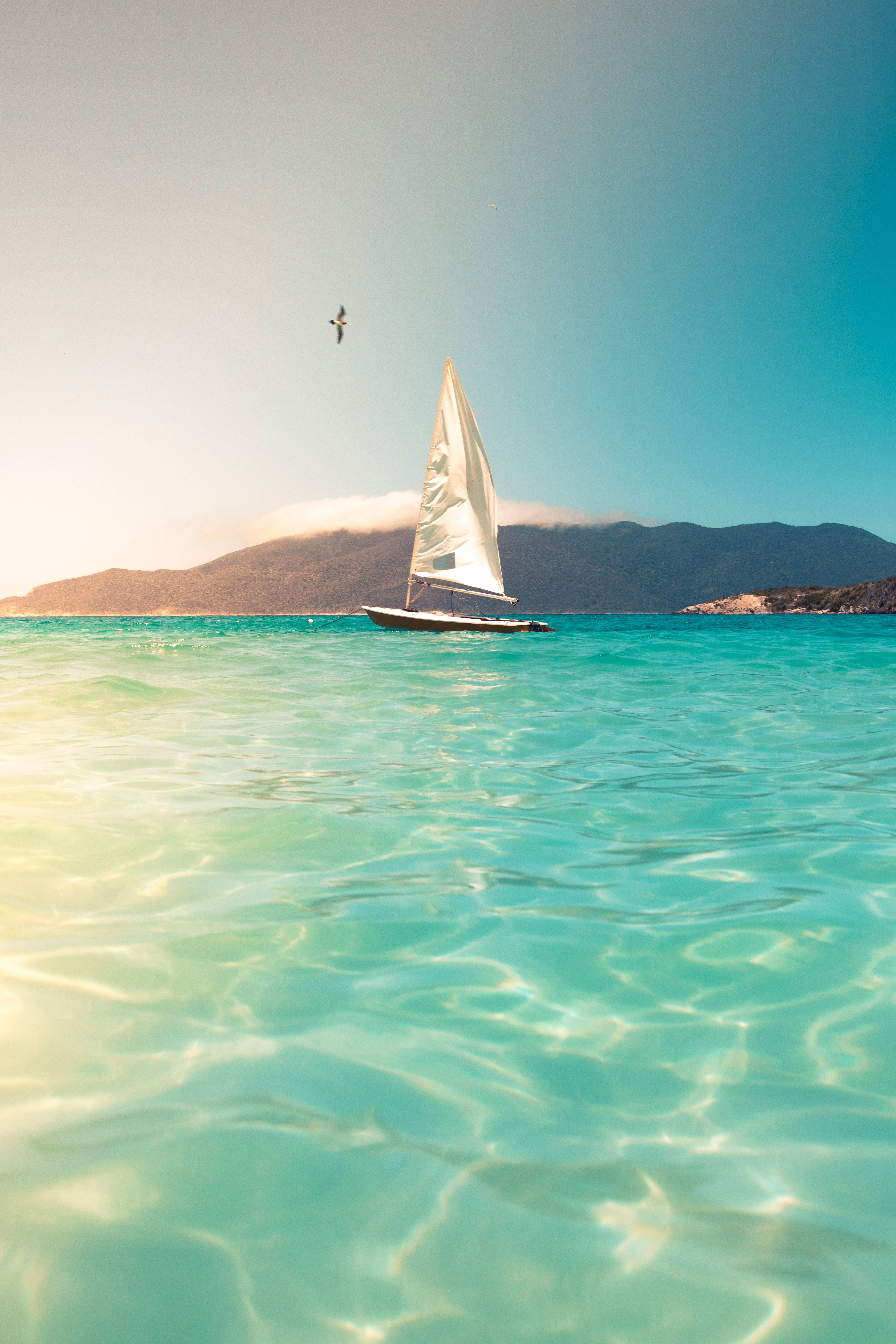 small sailboat, crystal turquoise waters, distant mountains, 5K Phone Wallpaper