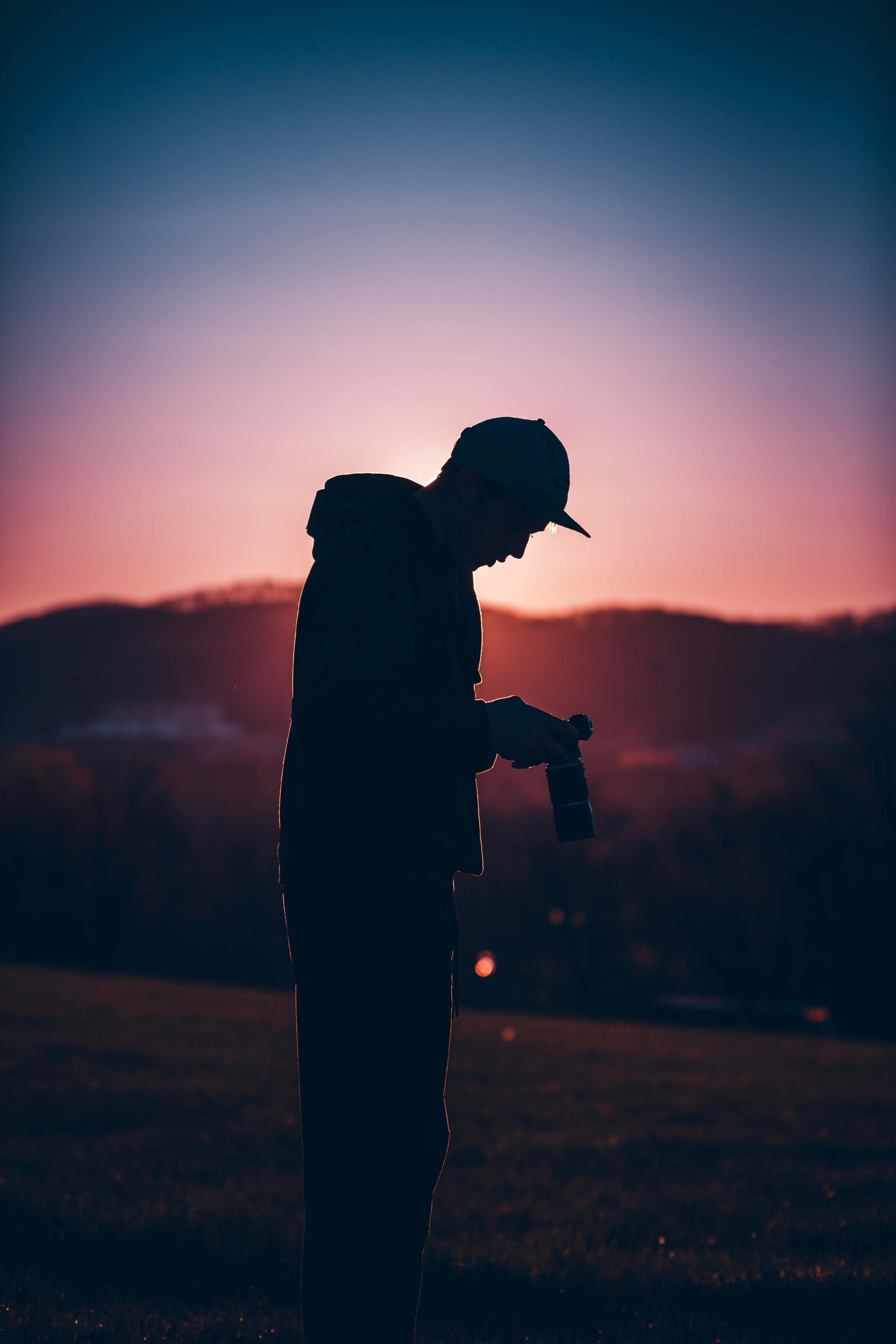 silhouetted photographer, vibrant pink and blue sunset, rolling hills, 5K Phone Wallpaper