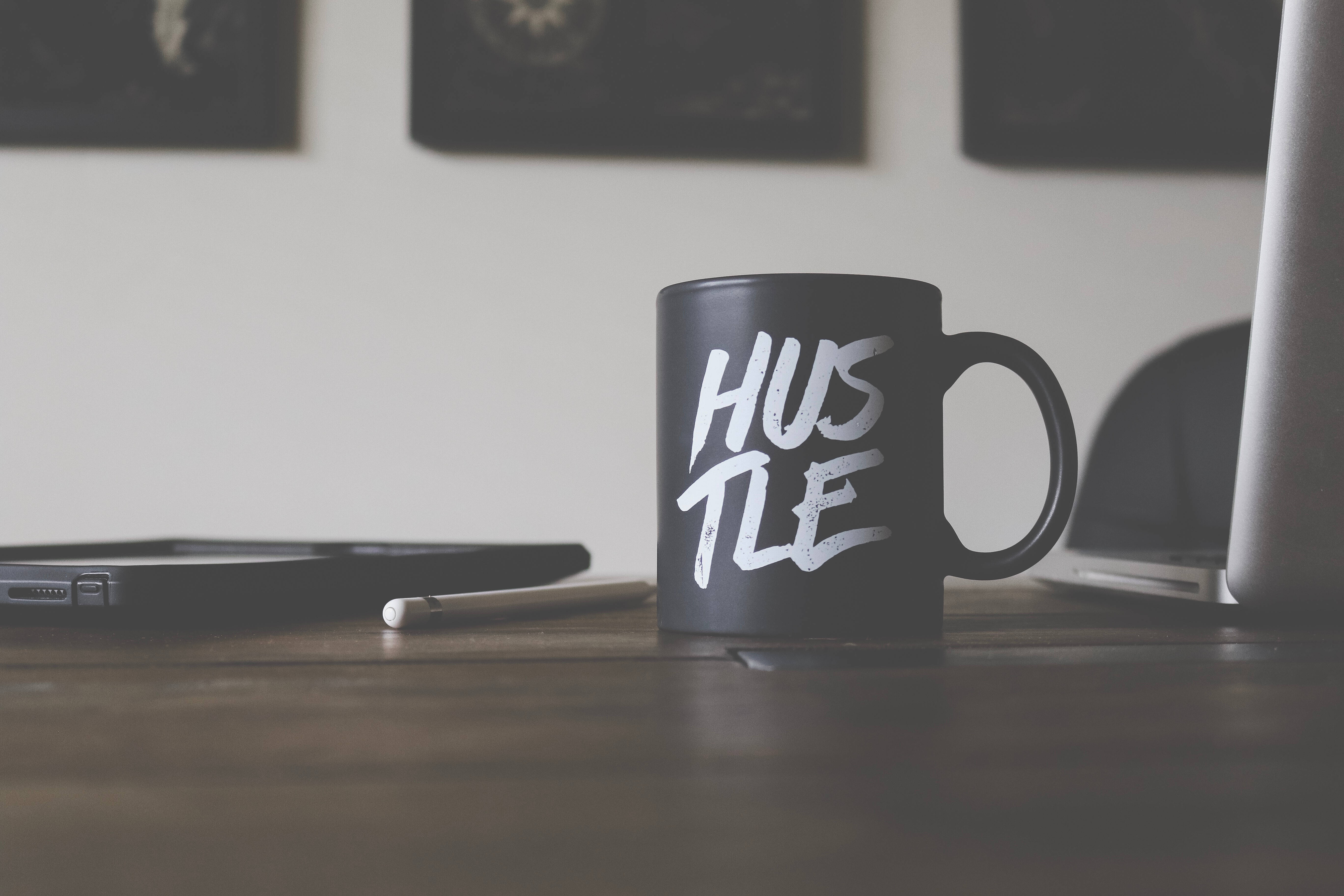 black mug, white 'HUSTLE' lettering, wooden desk, 5K Desktop Wallpaper