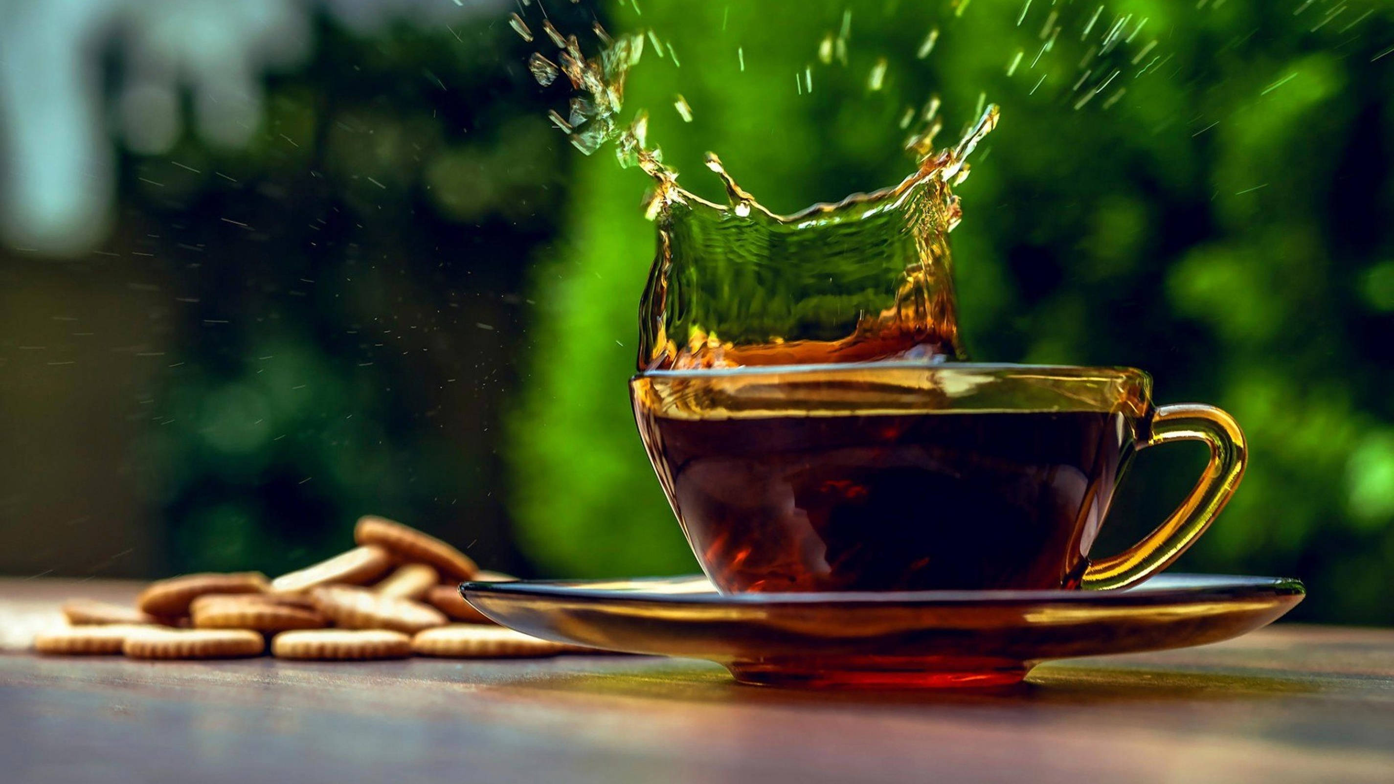 golden teacup, dark liquid, lush green blurred background, 2K Desktop Wallpaper