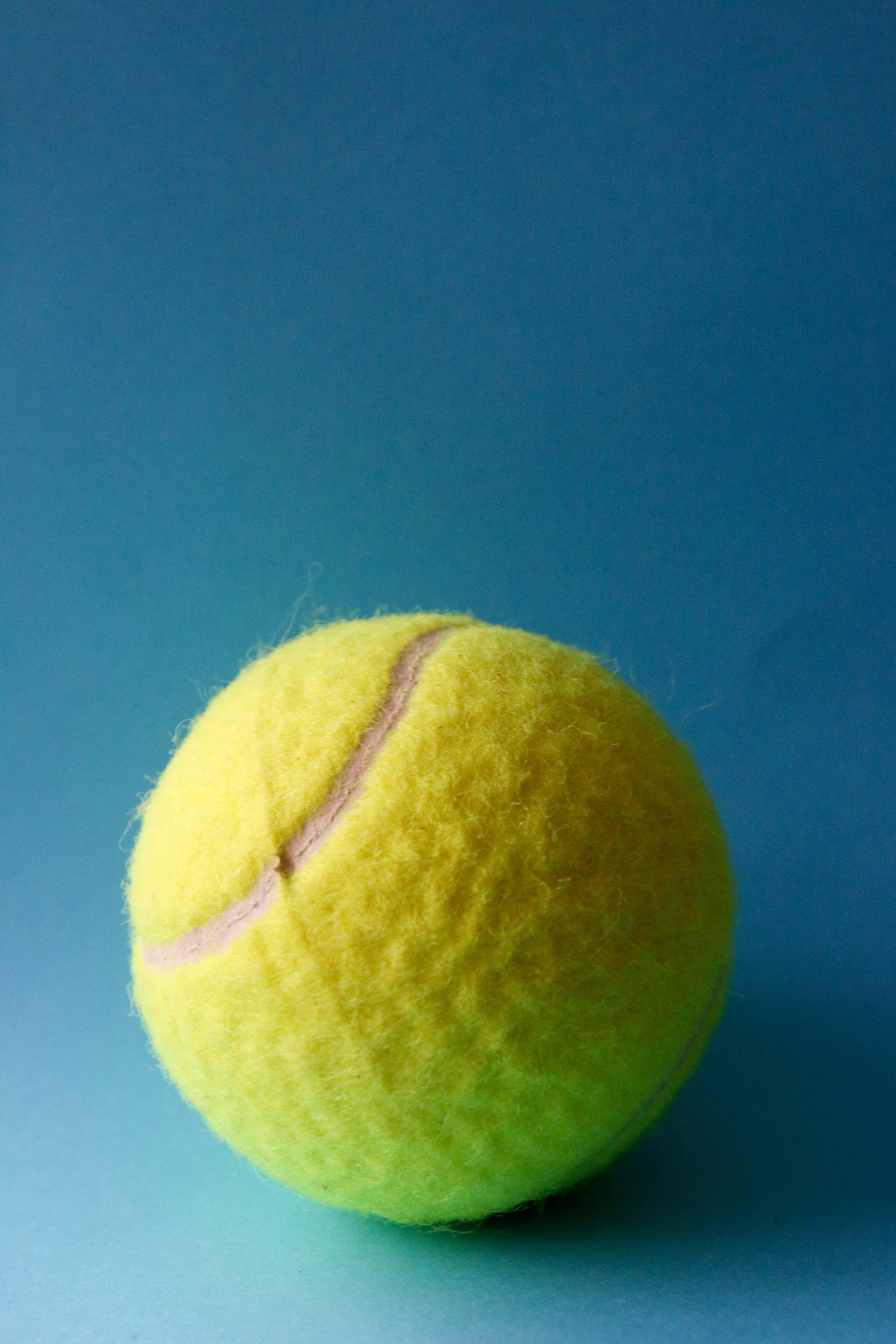 yellow tennis ball, solid blue background, soft lighting, 5K Phone Wallpaper