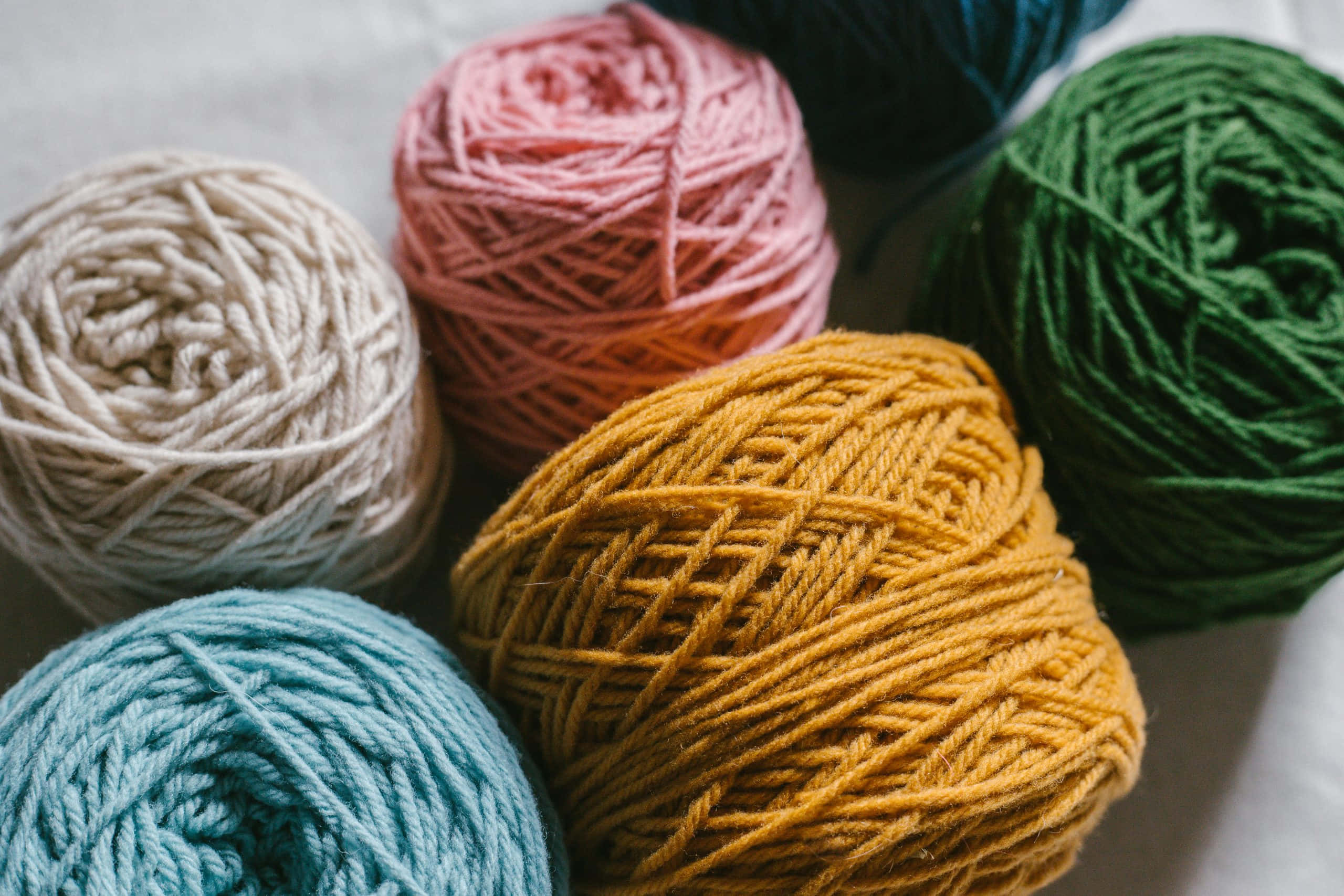 colorful yarn balls, cream pink mustard green and teal, soft white surface, 2K Desktop Wallpaper