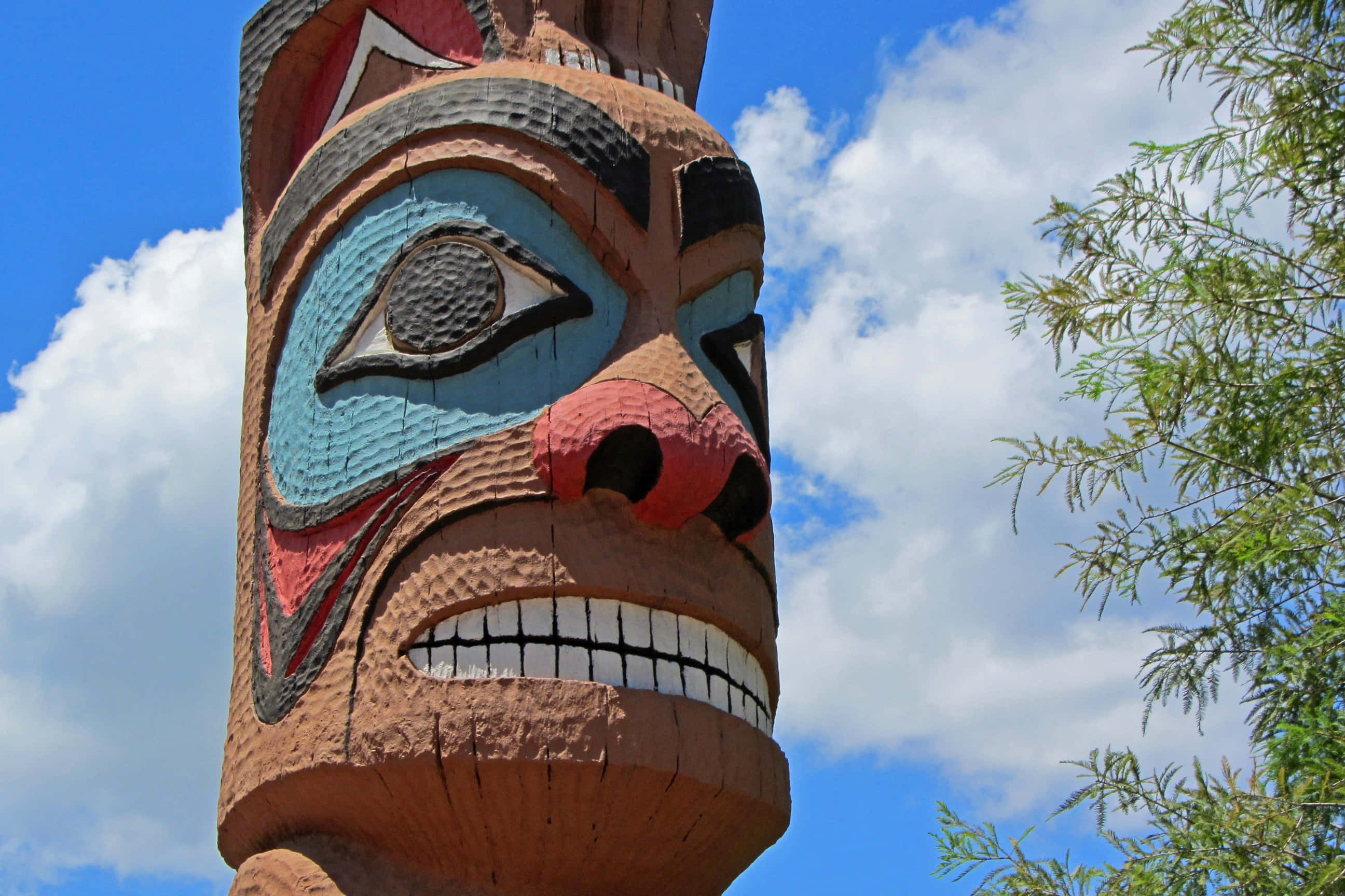 Colorful Tiki Totem Pole, bright blue sky, fluffy white clouds, 2K Desktop Wallpaper