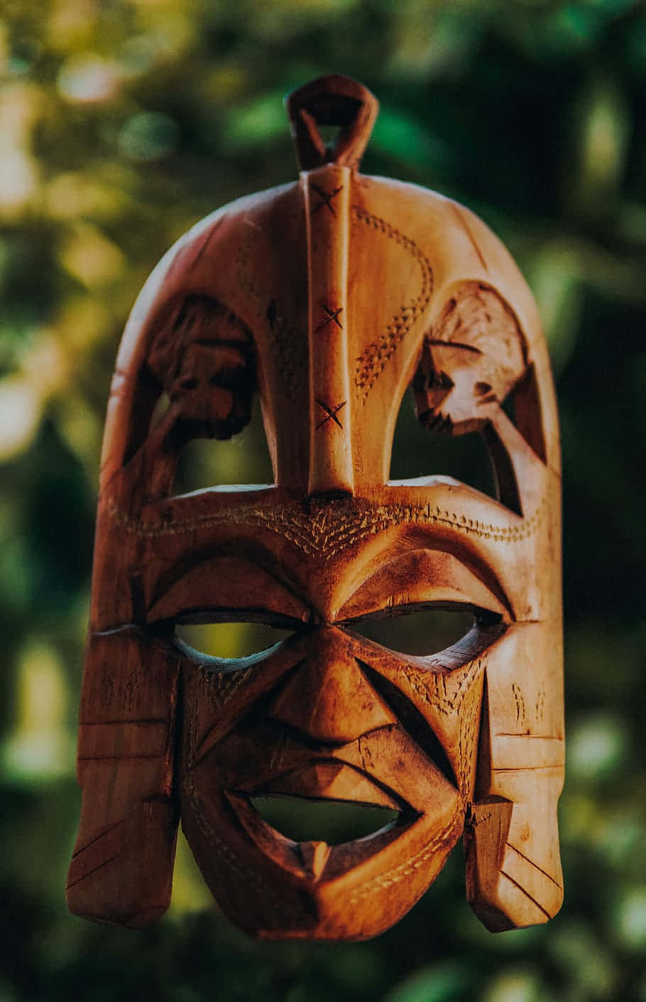 carved wooden tiki mask, fierce facial expression, soft green foliage background, HD Phone Wallpaper