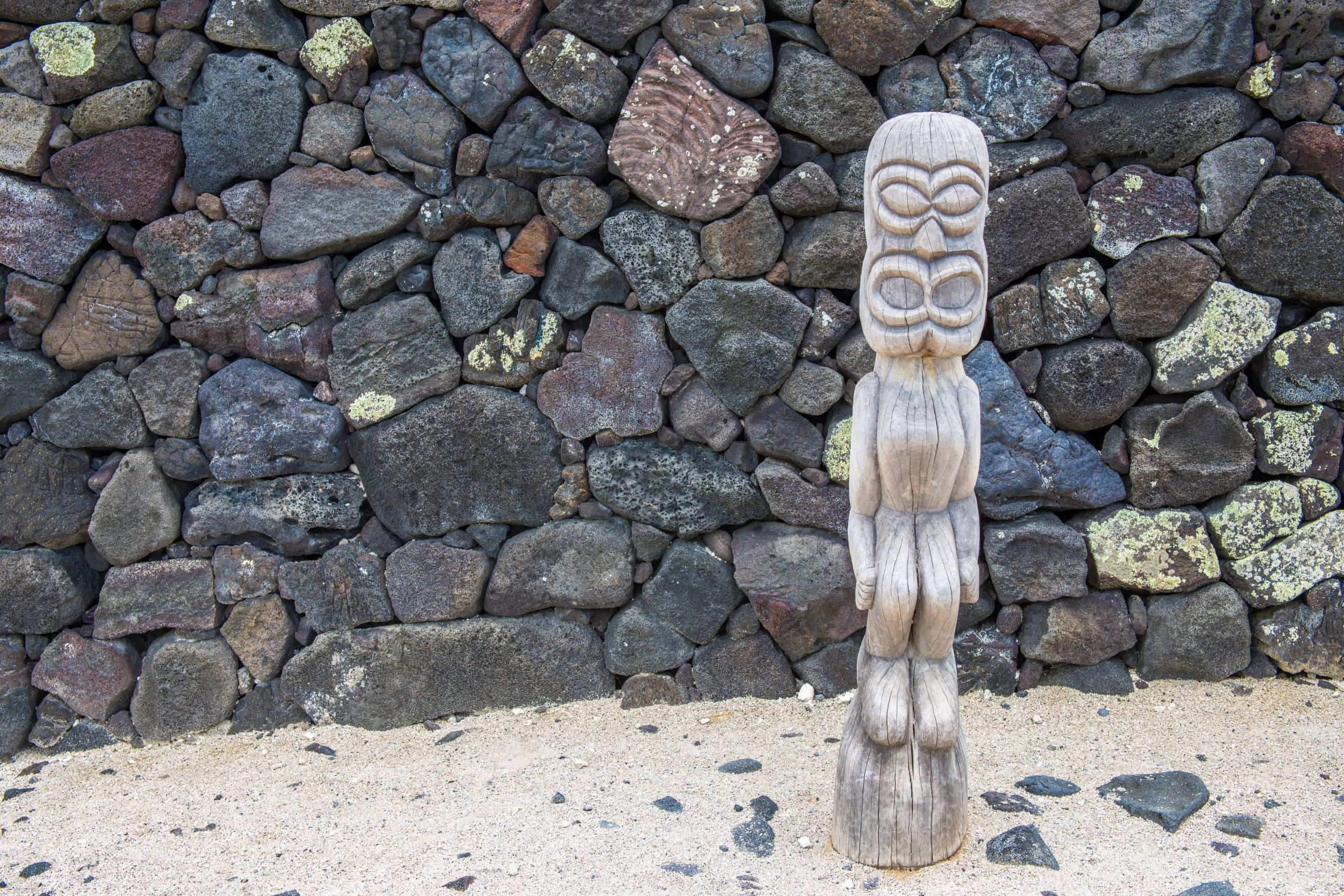 wooden tiki statue, rugged volcanic rock wall, bright daylight, 2K Desktop Wallpaper