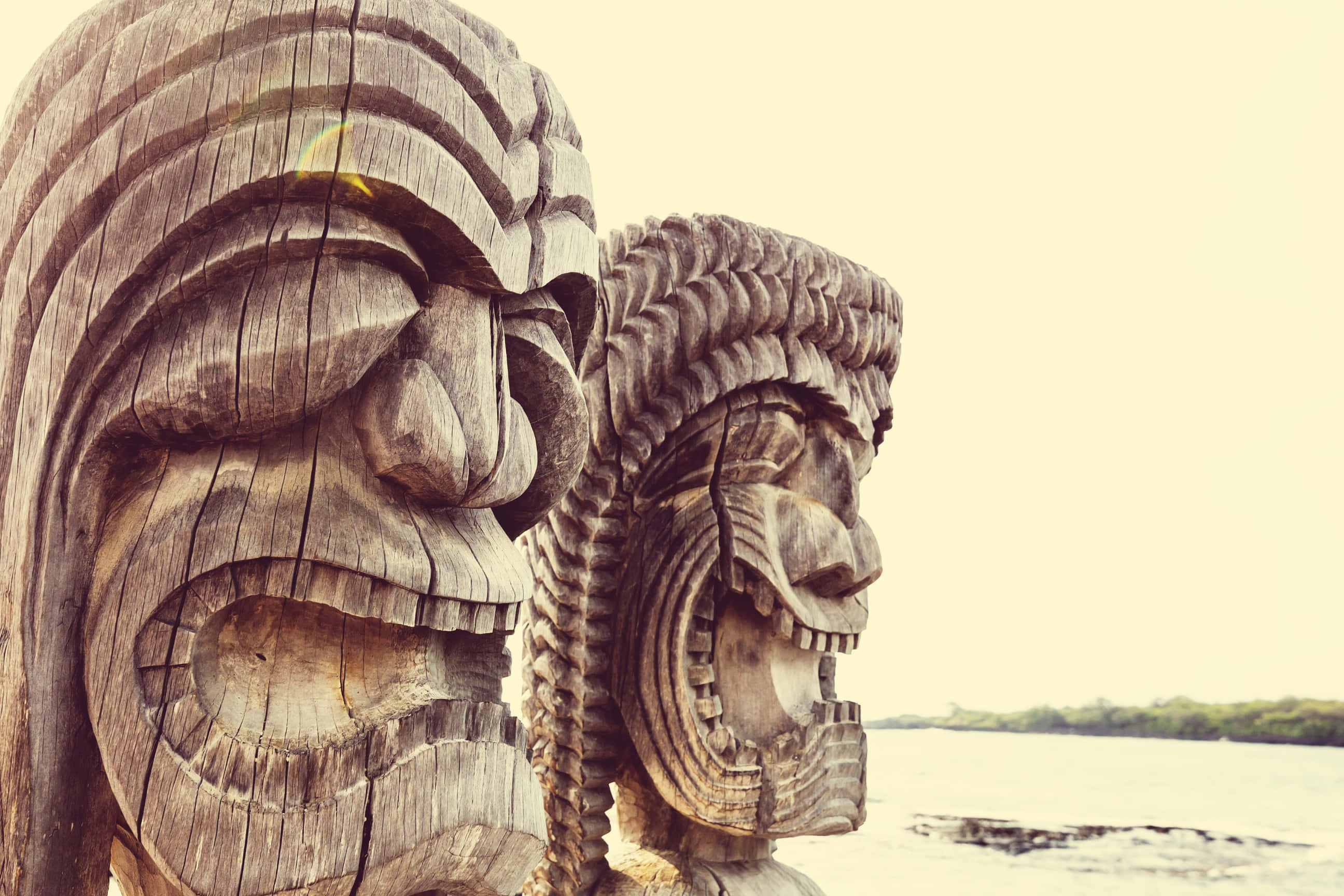 carved wooden tiki statues, seaside, weathered wooden tiki masks, 2K Desktop Wallpaper