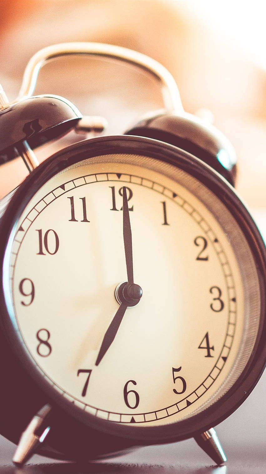 vintage black alarm clock, hands pointing to 7:00, warm golden light, HD Phone Wallpaper