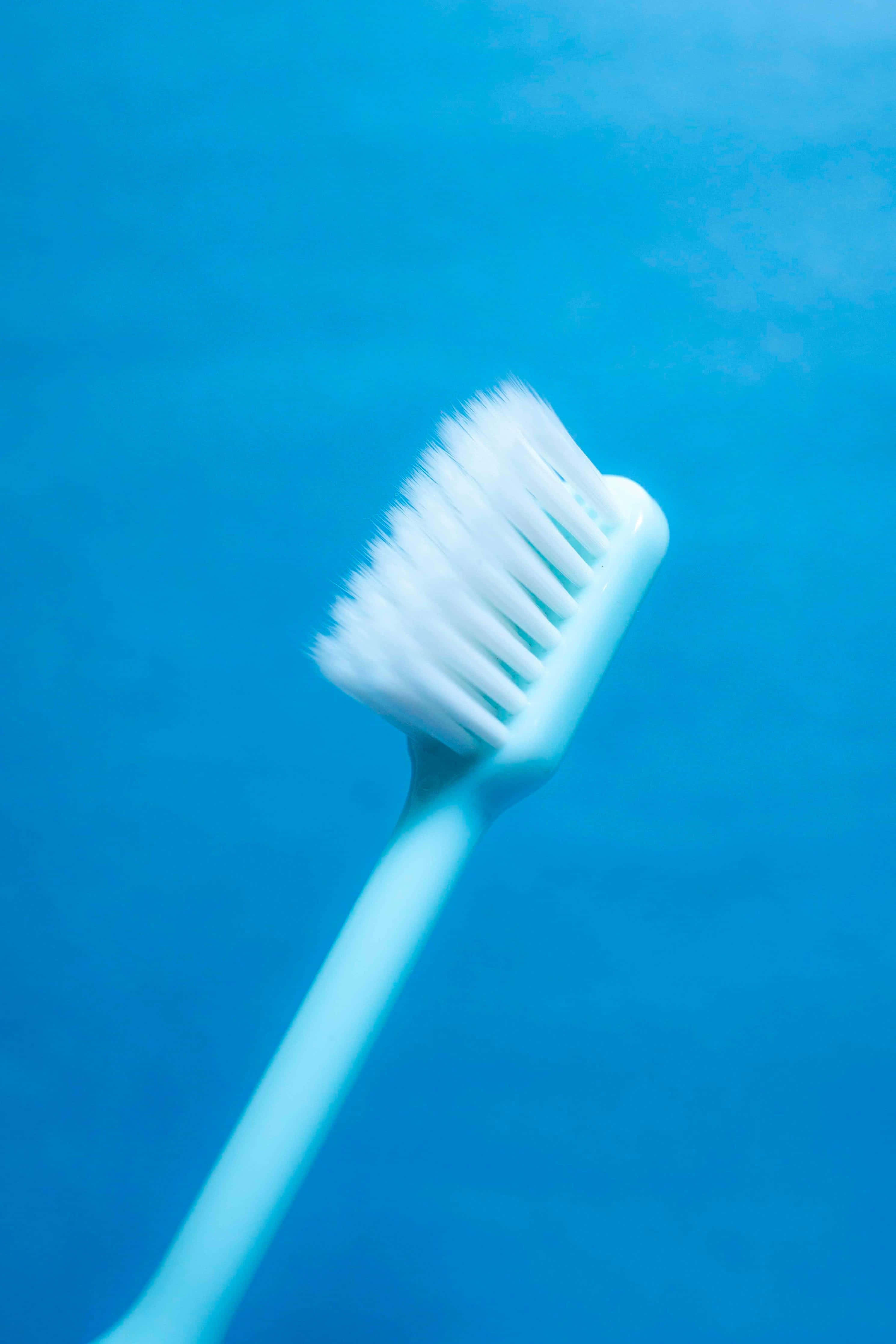 white toothbrush, bristles angled upward, solid blue background, 4K Phone Wallpaper