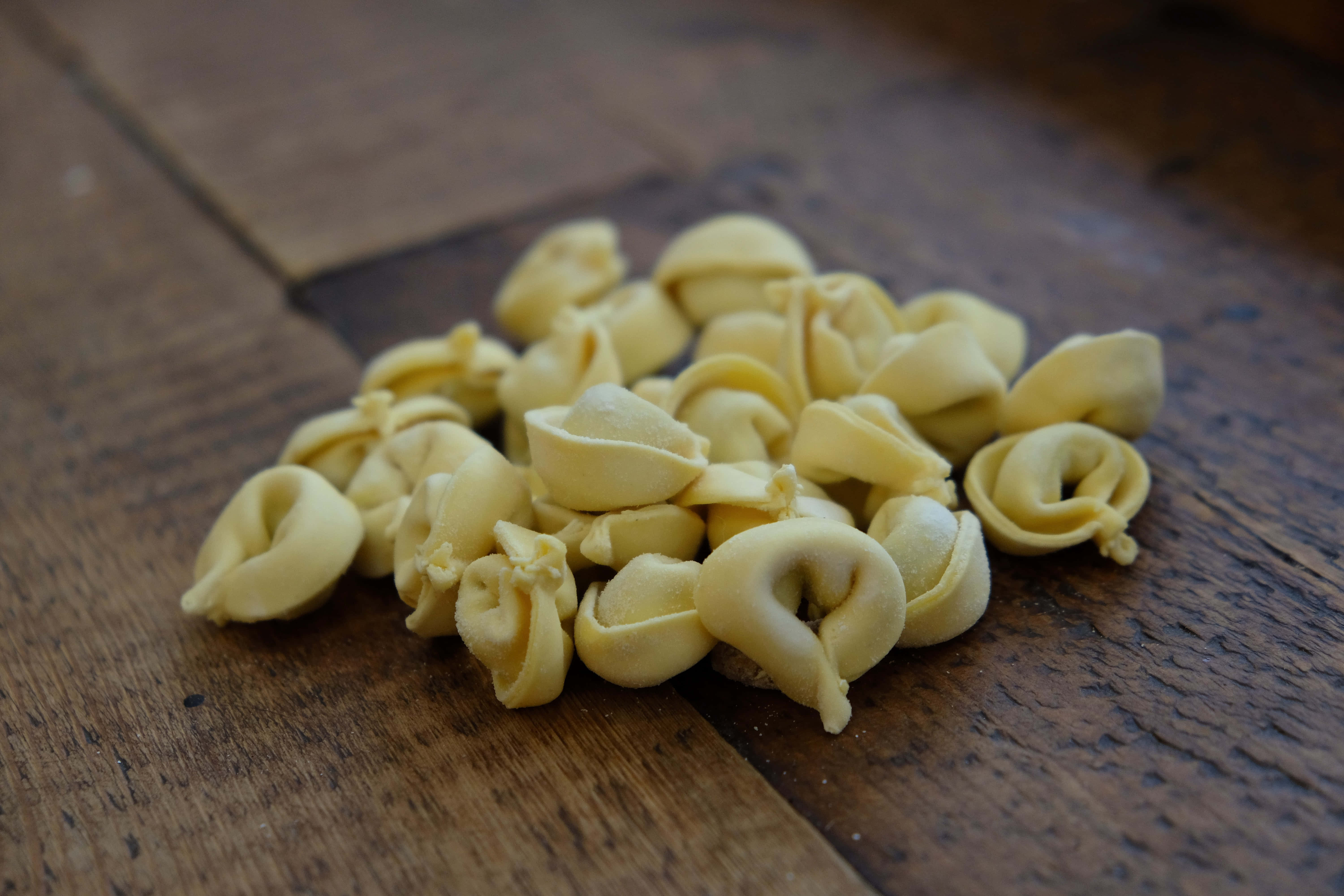 tortellini in brodo, pale yellow tortellini pasta, rustic wooden surface, 5K Desktop Wallpaper