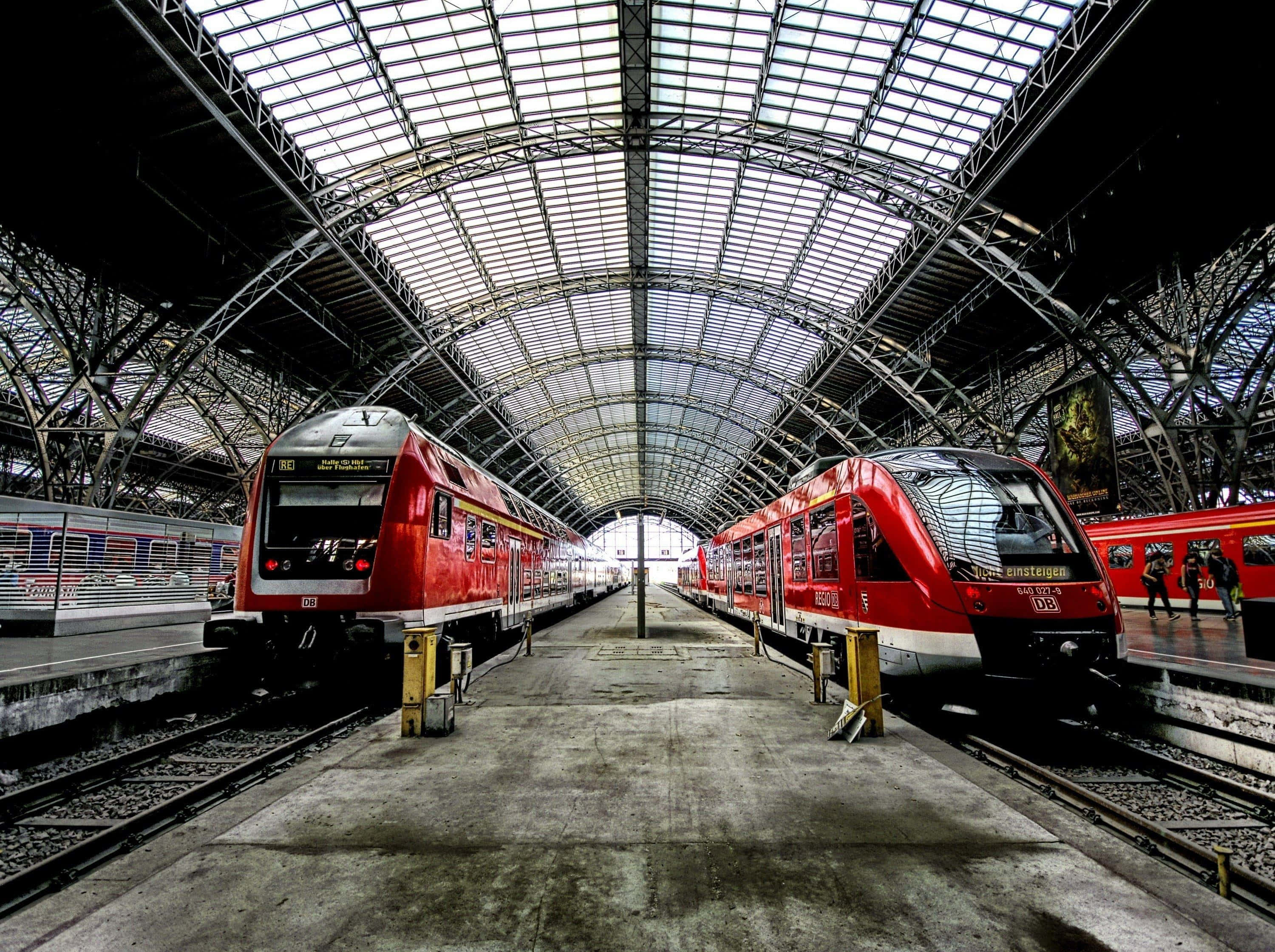 modern train station platform, red trains, vast arched glass and steel station roof, 2K Desktop Wallpaper