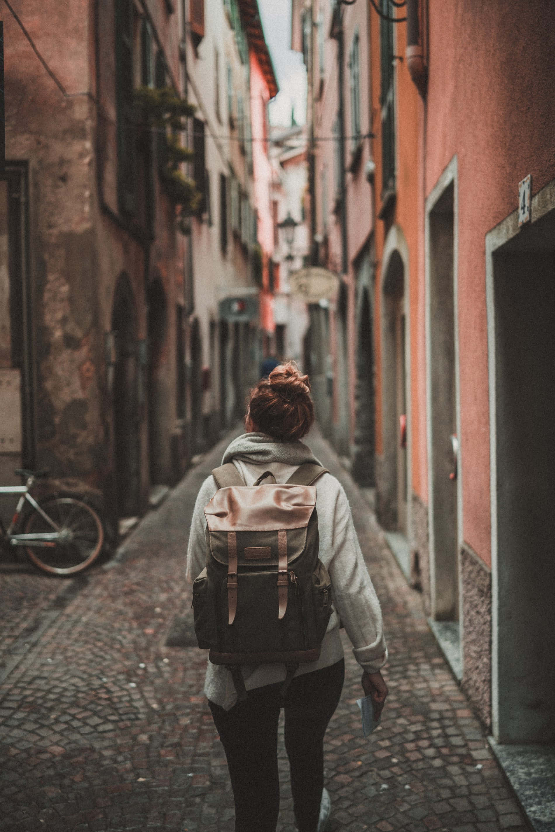narrow cobblestone alley, warm-toned historic buildings, woman walking, 2K Phone Wallpaper