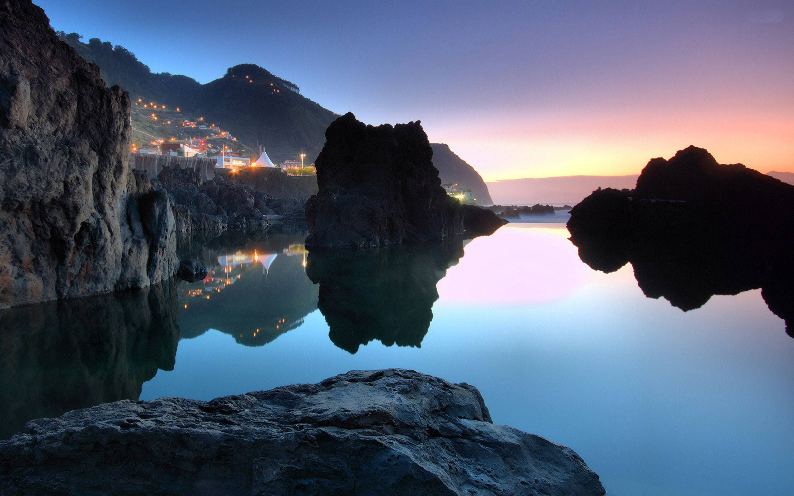 twilight coastal scene, glowing village lights, calm turquoise waters, 2K Desktop Wallpaper