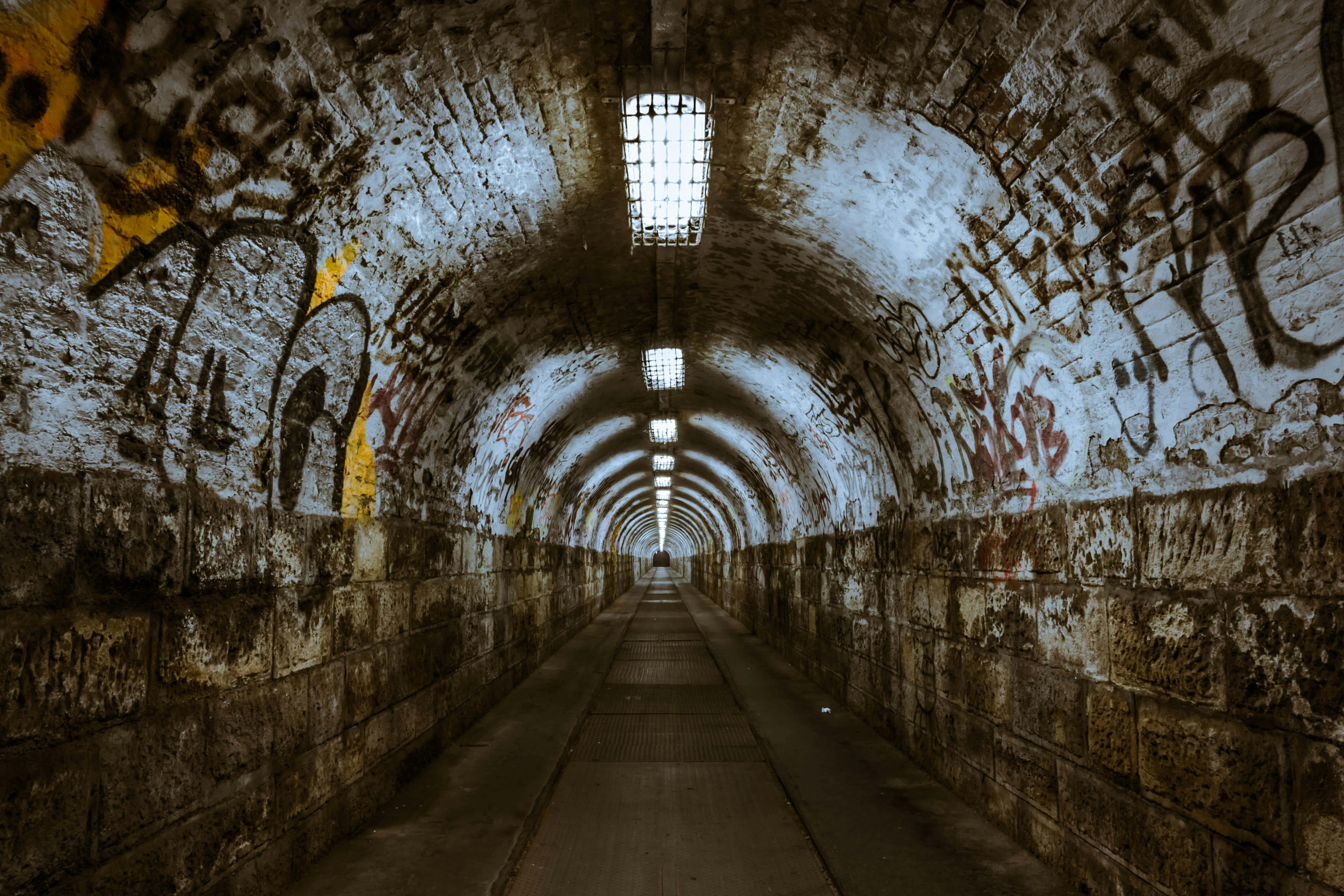 graffiti adorned tunnel, arched brick tunnel, flickering overhead lights, 5K Desktop Wallpaper