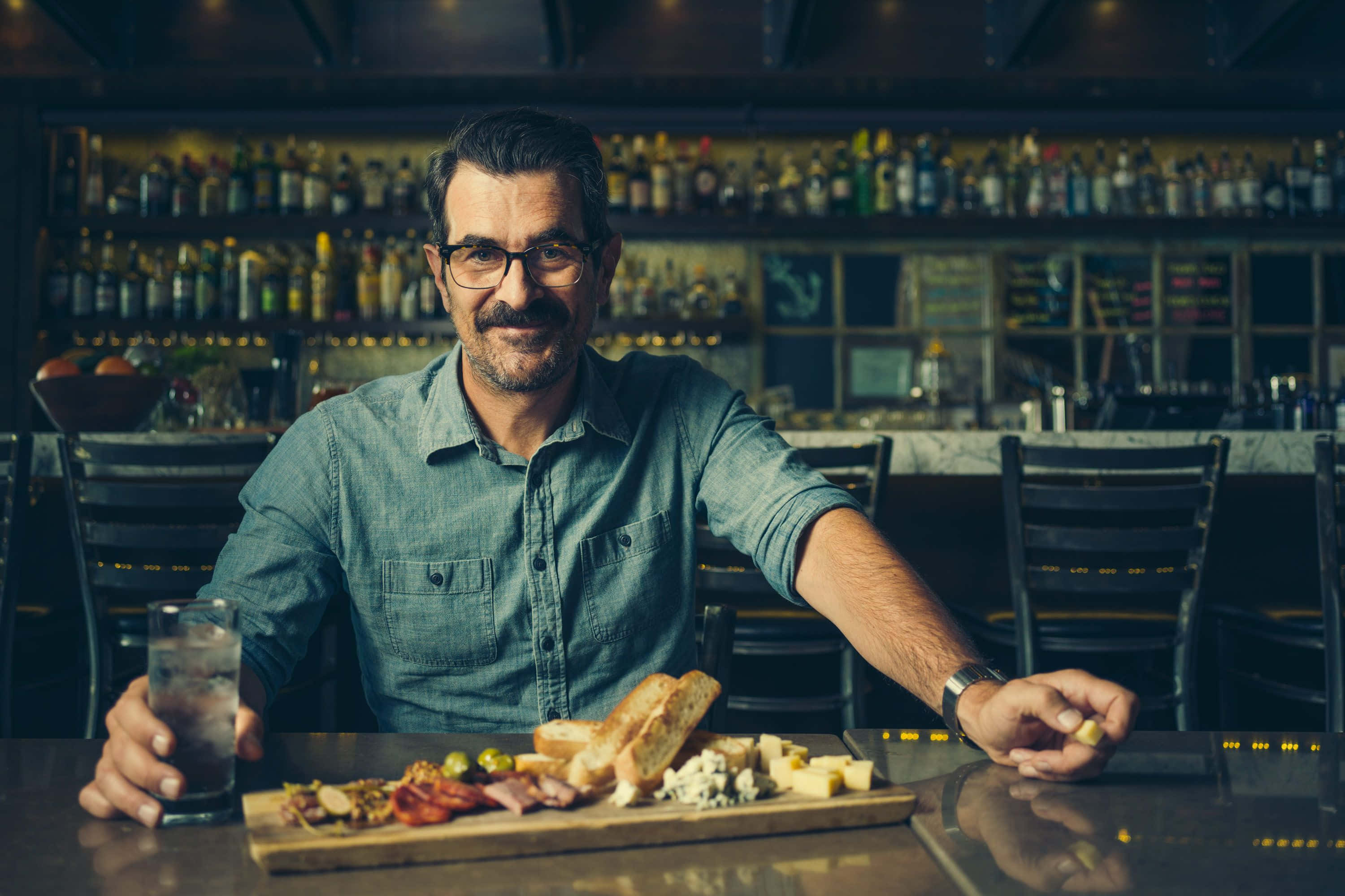 Ty Burrell, charcuterie board, dimly lit bar, 2K Desktop Wallpaper