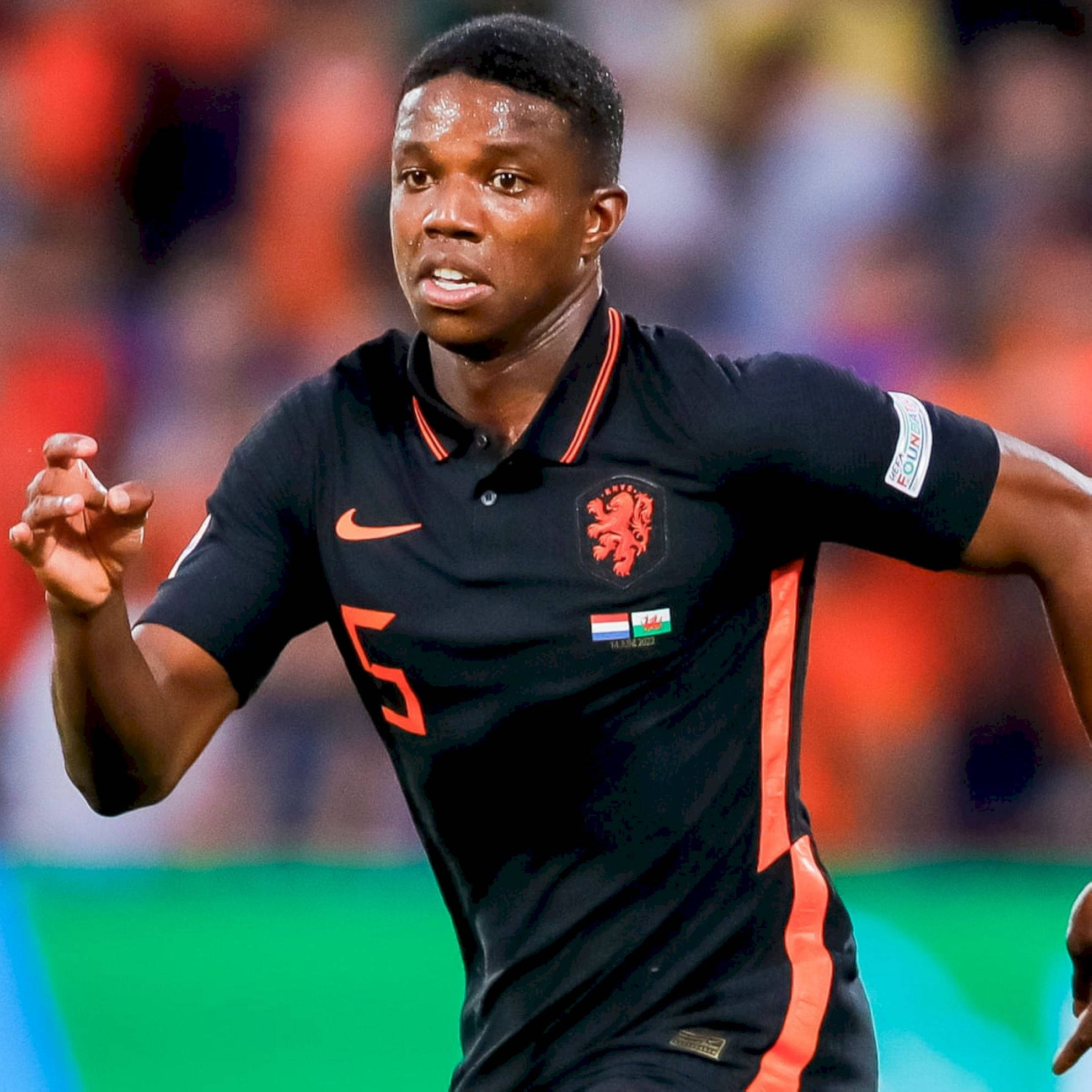 Tyrell Malacia, black and orange jersey, vibrant green pitch, Full HD Desktop Wallpaper