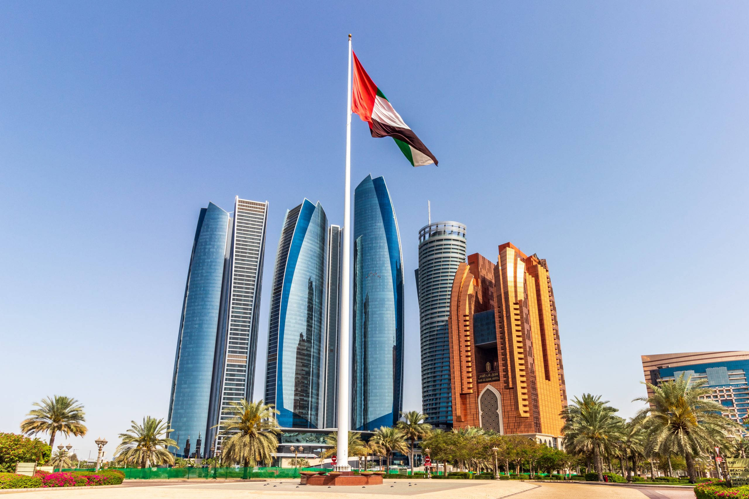 UAE flag, clear blue sky, modern glass skyscrapers, 2K Desktop Wallpaper