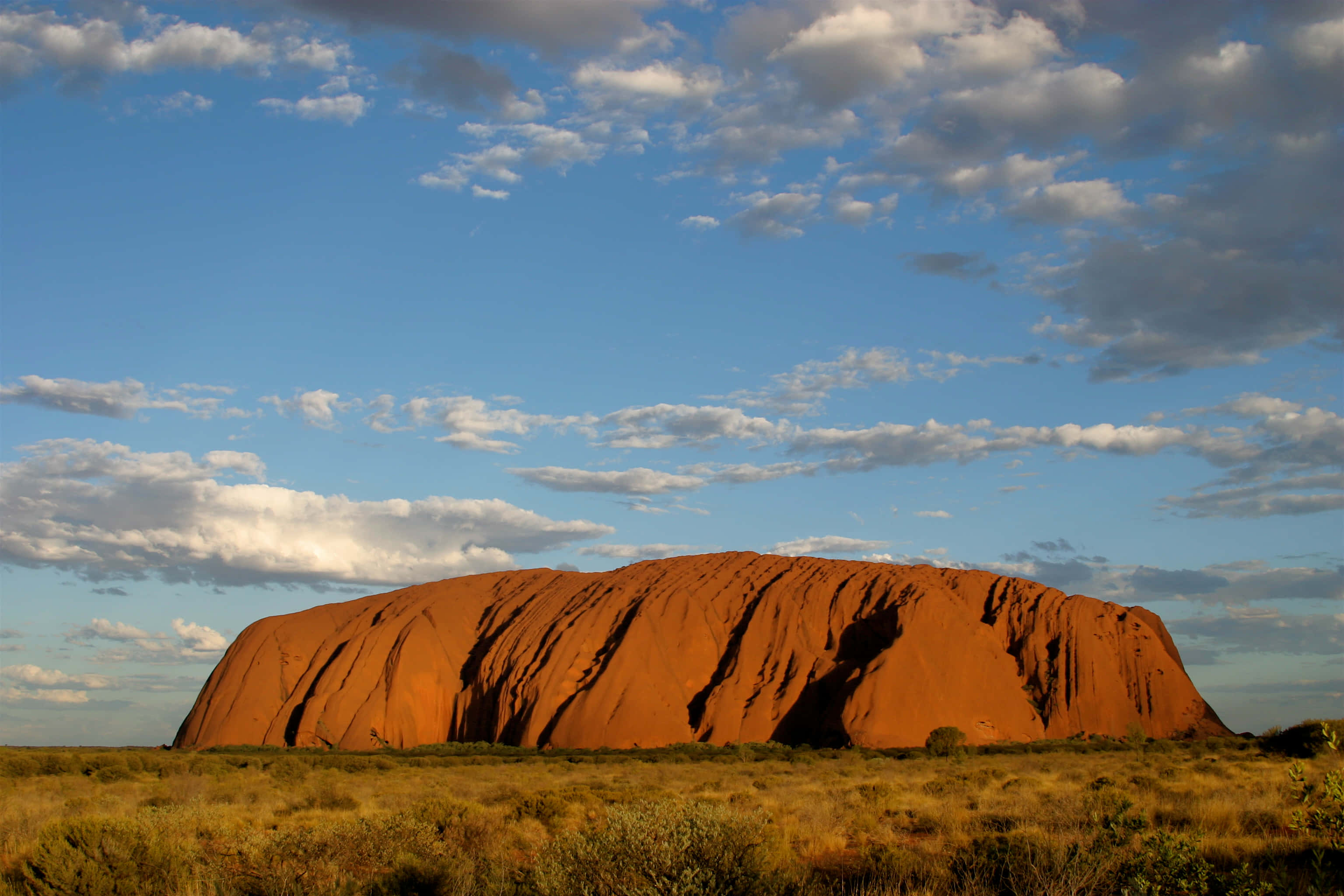 Uluru, red rock formation, arid golden grasslands, 2K Desktop Wallpaper