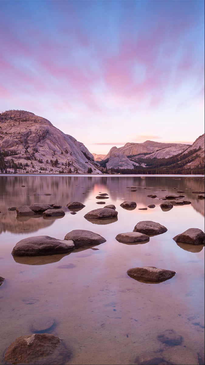 Pink and purple sunset sky, calm lake water, smooth rocks, SD Phone Wallpaper