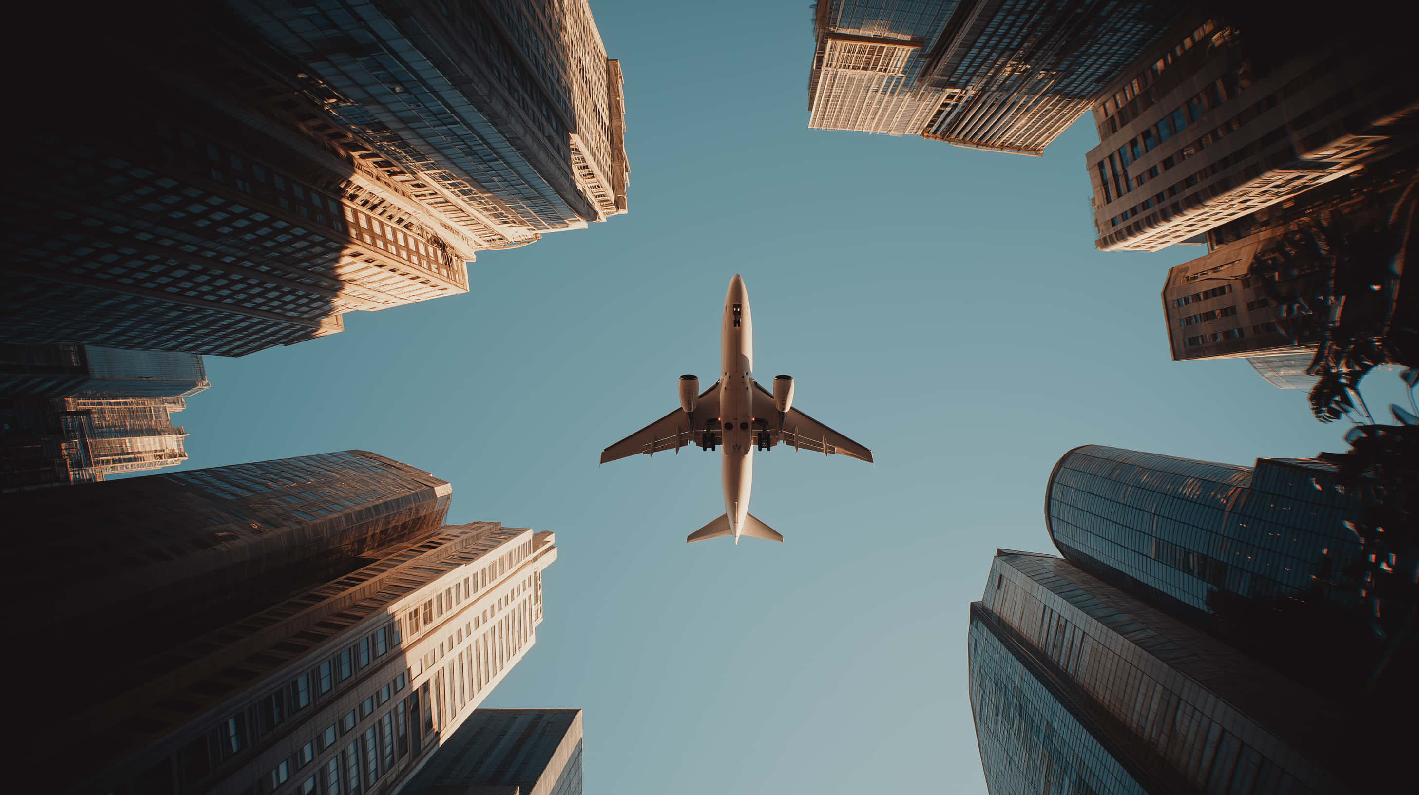 commercial airplane, clear blue sky, towering glass and steel skyscrapers, 2K Desktop Wallpaper