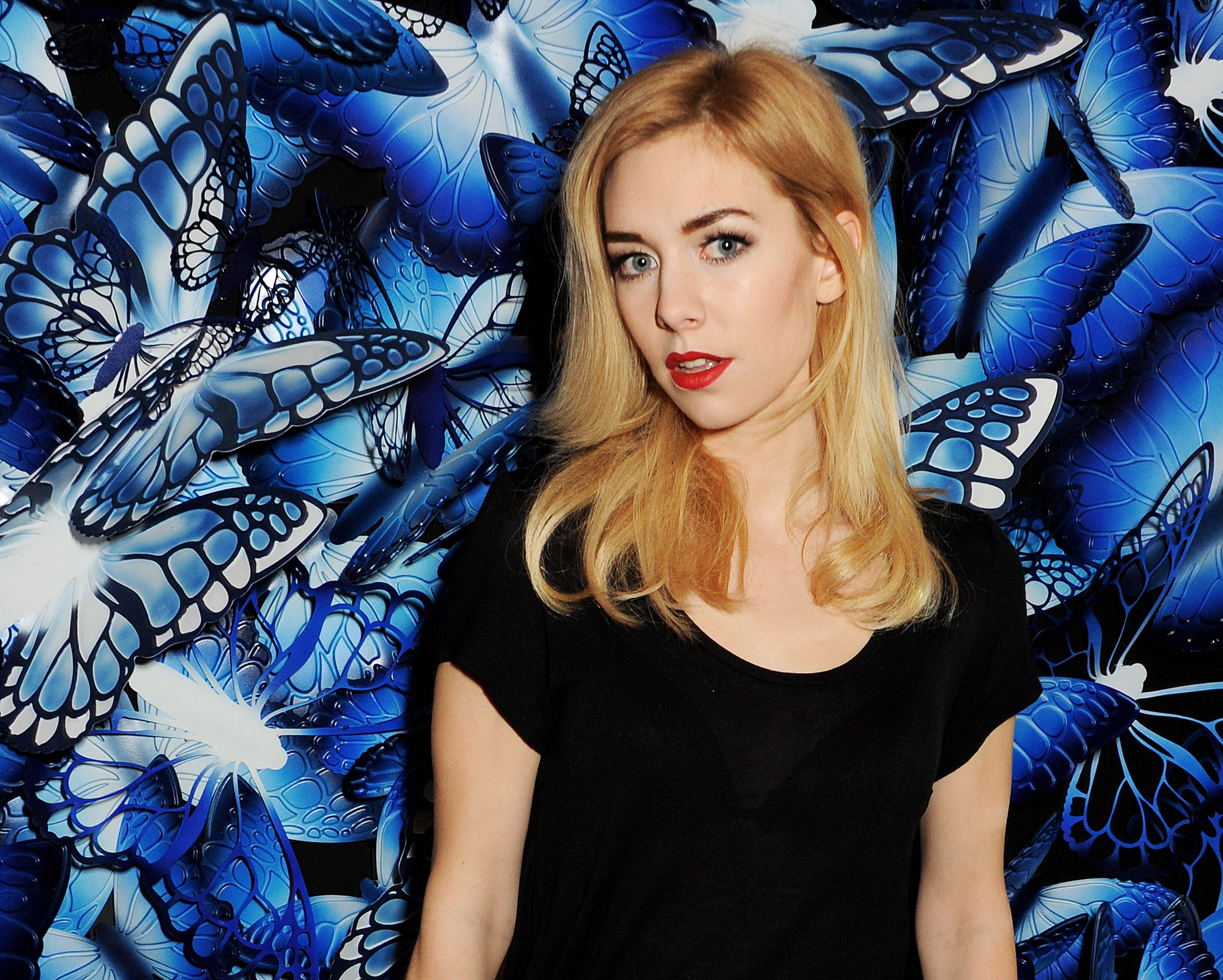 Vanessa Kirby, black top, vibrant blue butterfly-patterned wall, 2K Desktop Wallpaper
