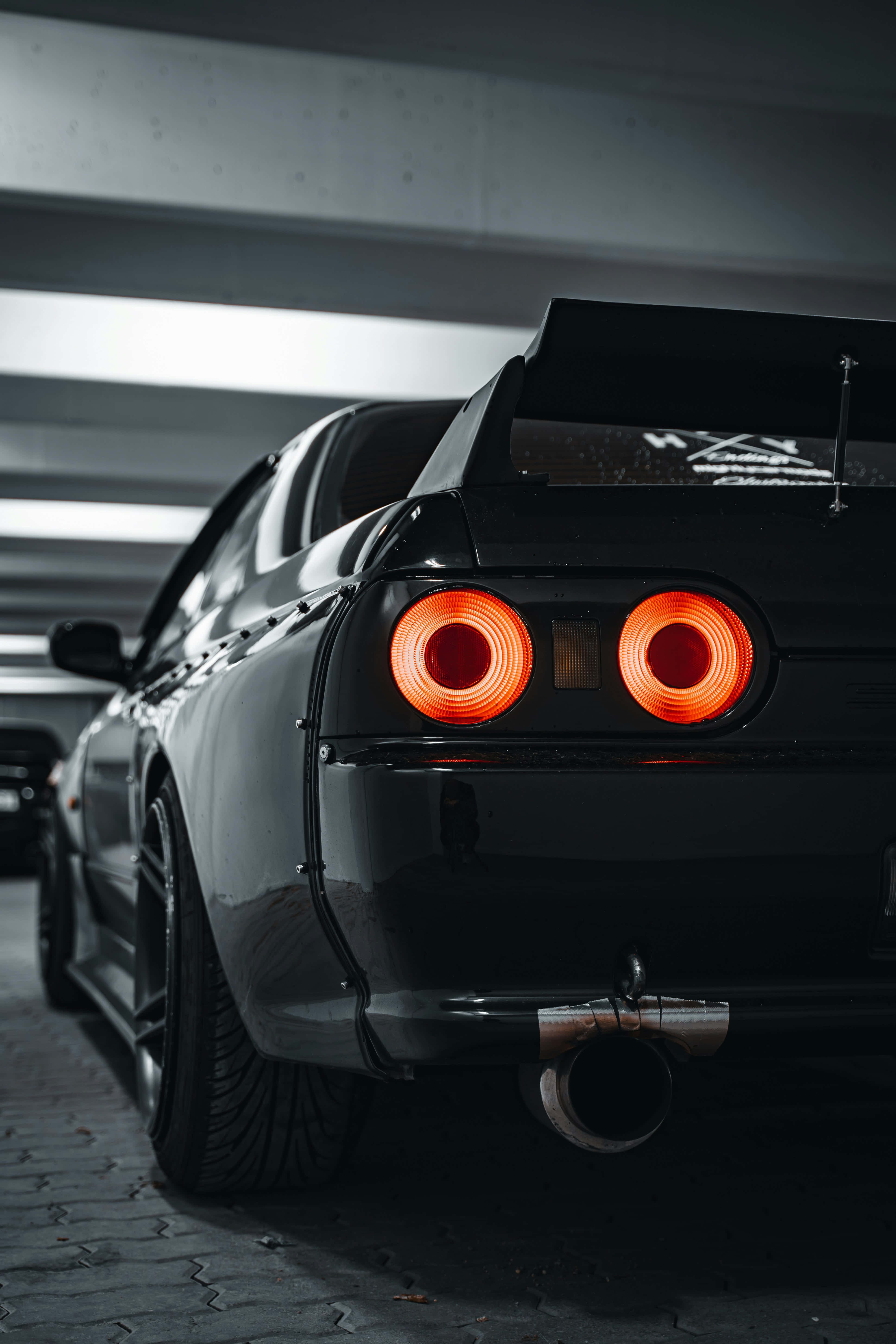 black sports car, glowing orange taillights, dimly lit underground parking garage, 5K Phone Wallpaper