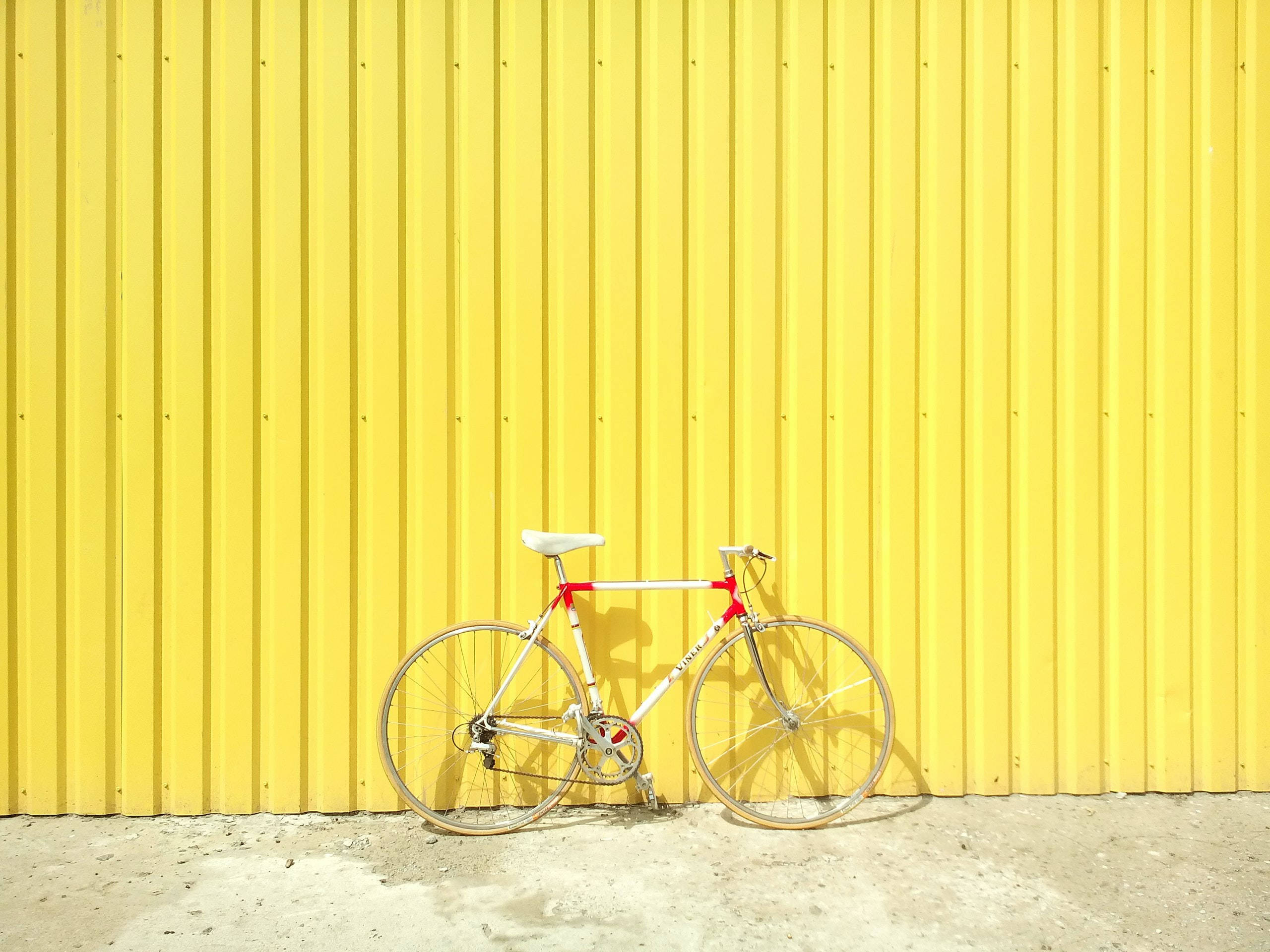 white and red bicycle, bright yellow corrugated metal wall, concrete ground, 2K Desktop Wallpaper