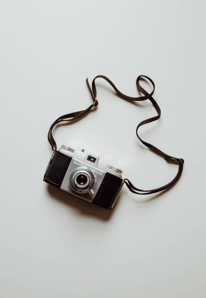 vintage silver and black film camera, brown strap, plain white surface, SD Phone Wallpaper