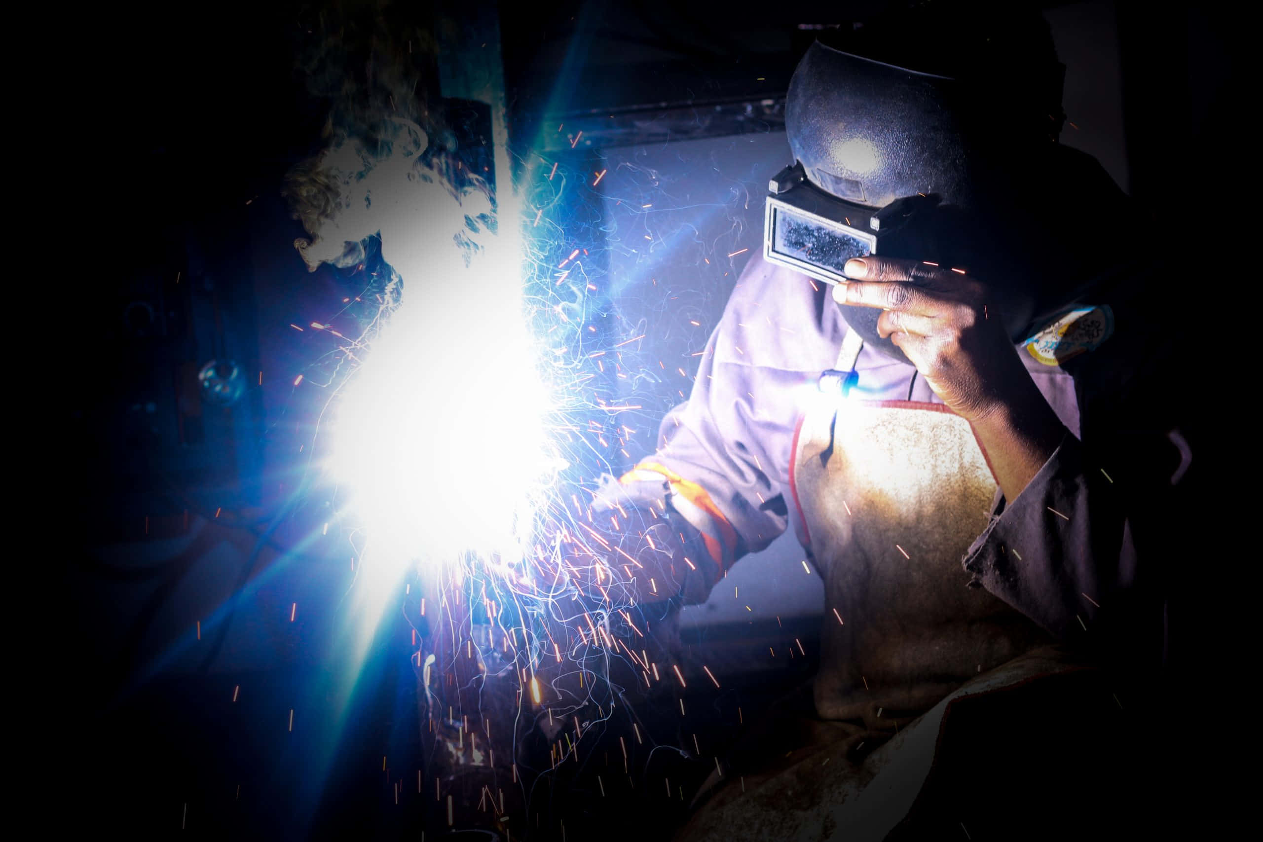 welder, dark workshop, blue and orange sparks, 2K Desktop Wallpaper