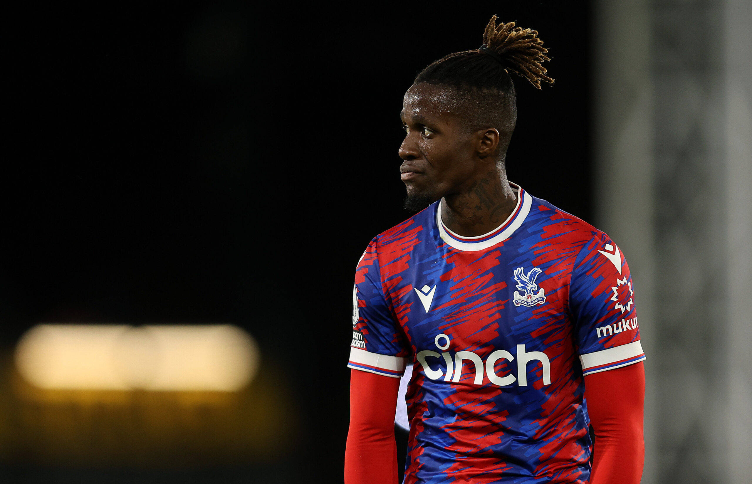 Wilfried Zaha, red and blue patterned jersey, dark stadium background, 2K Desktop Wallpaper