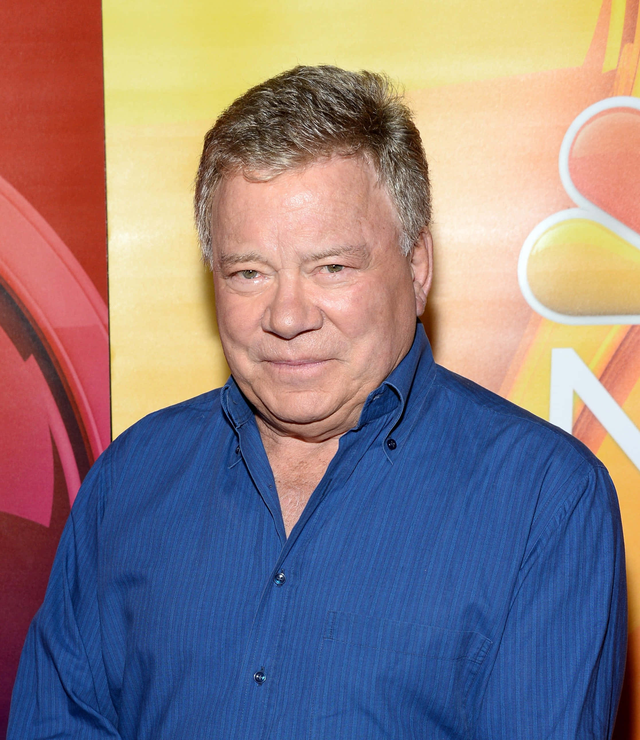 William Shatner, blue button-down shirt, colorful NBC logo backdrop, 2K Phone Wallpaper
