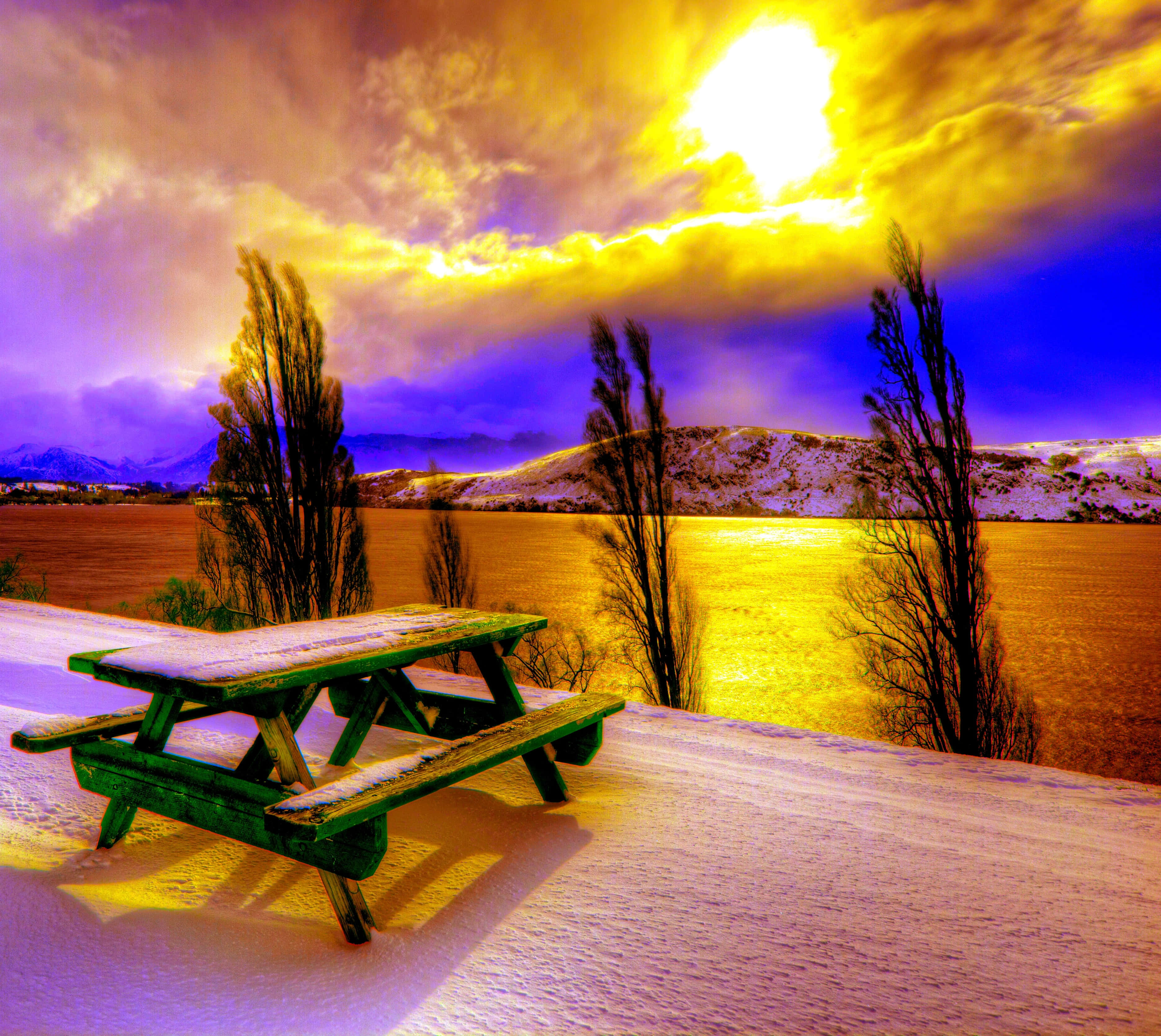 Winter Sun, snow-dusted green picnic table, golden sunset, 2K Desktop Wallpaper