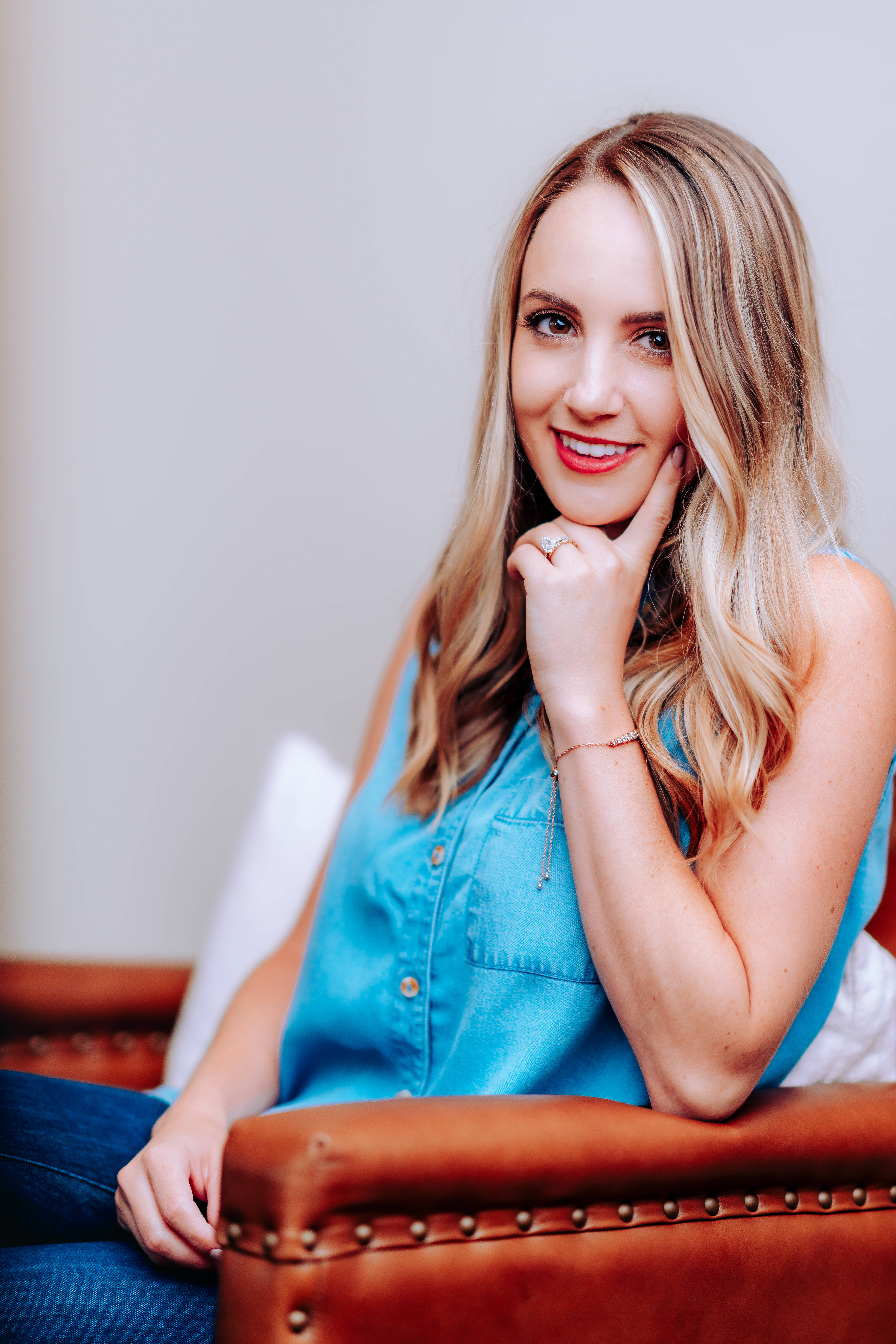 young blonde girl, blue top, brown leather couch, 8K Phone Wallpaper