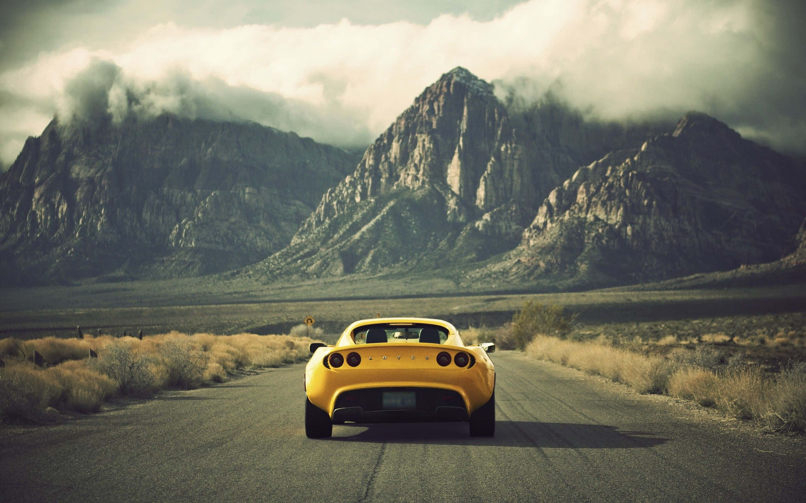 Sleek Yellow Sports Car, desert road, towering rocky mountains, 2K Desktop Wallpaper