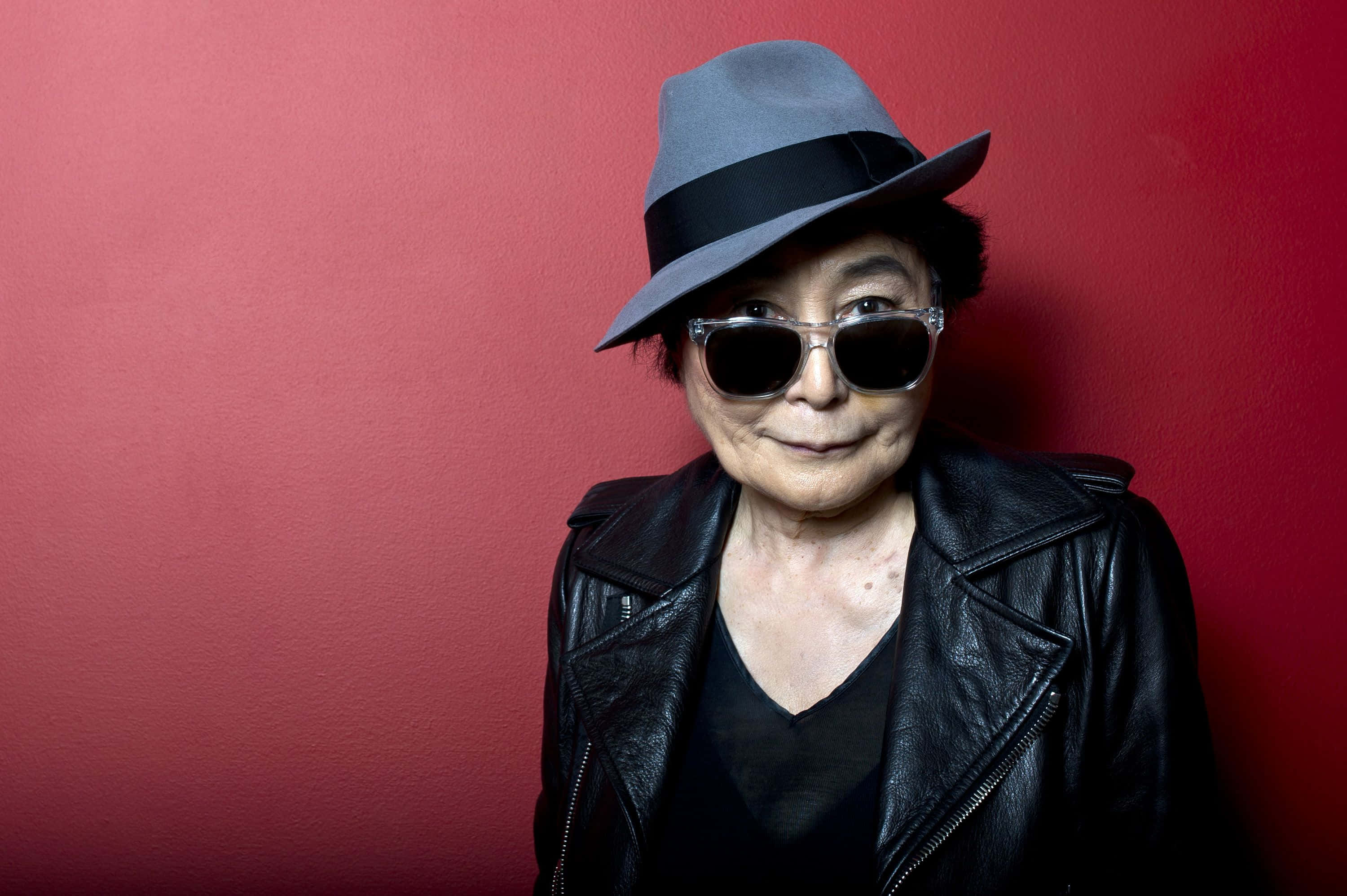 Yoko Ono, red background, grey fedora, 2K Desktop Wallpaper