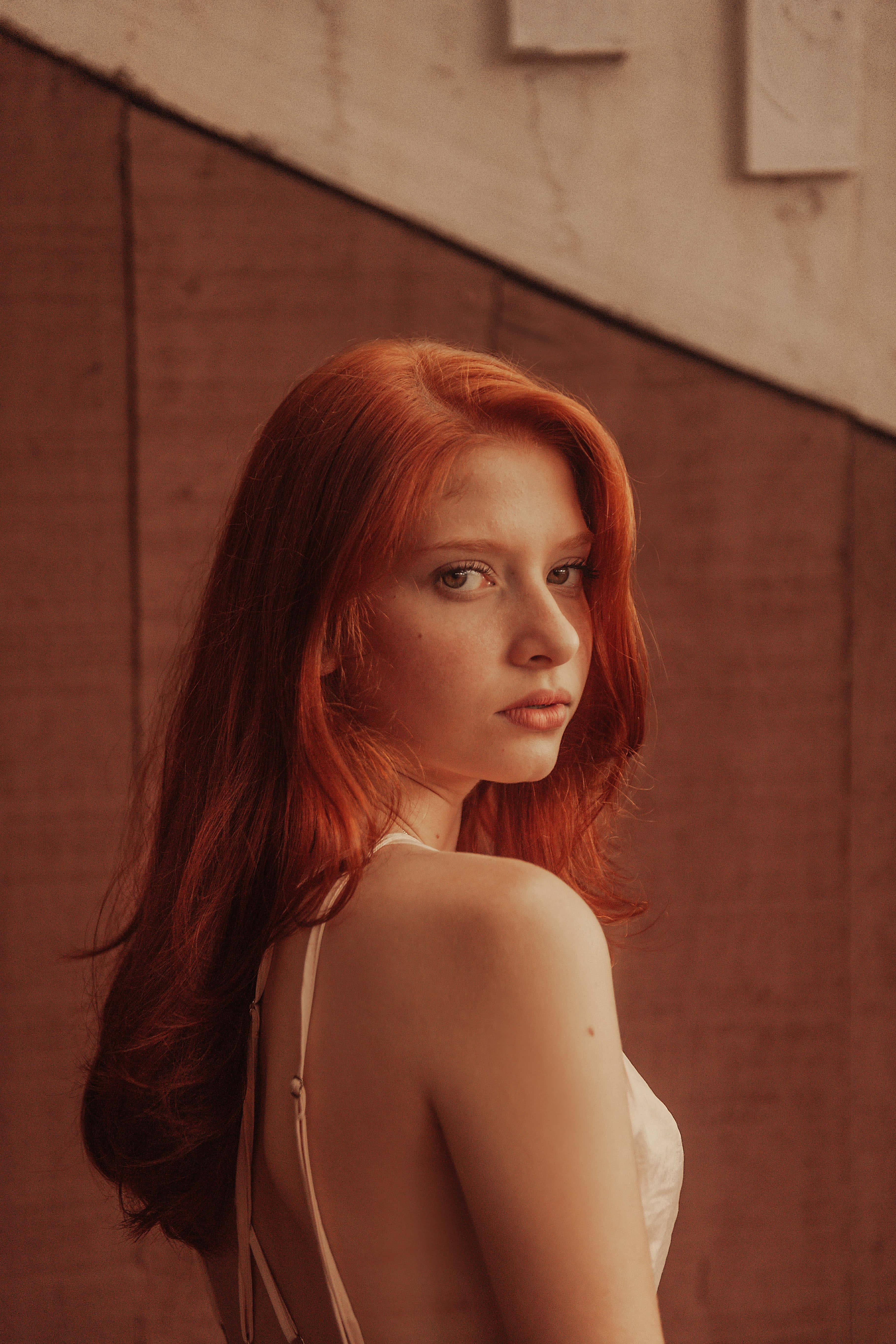 young female model, vibrant red hair, warm-toned textured wall, 5K Phone Wallpaper