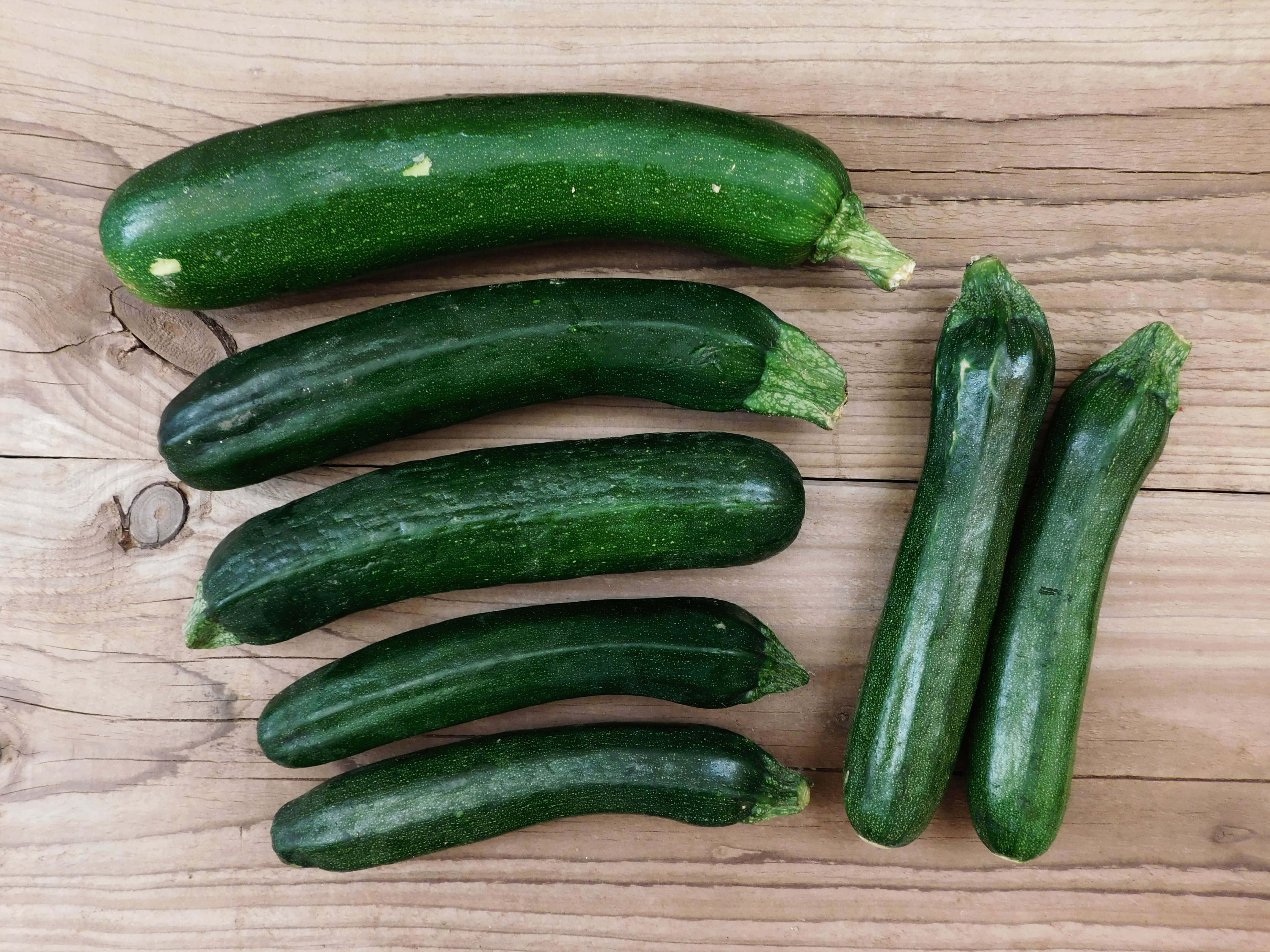 zucchinis, light brown wooden surface, visible grain, 4K Desktop Wallpaper